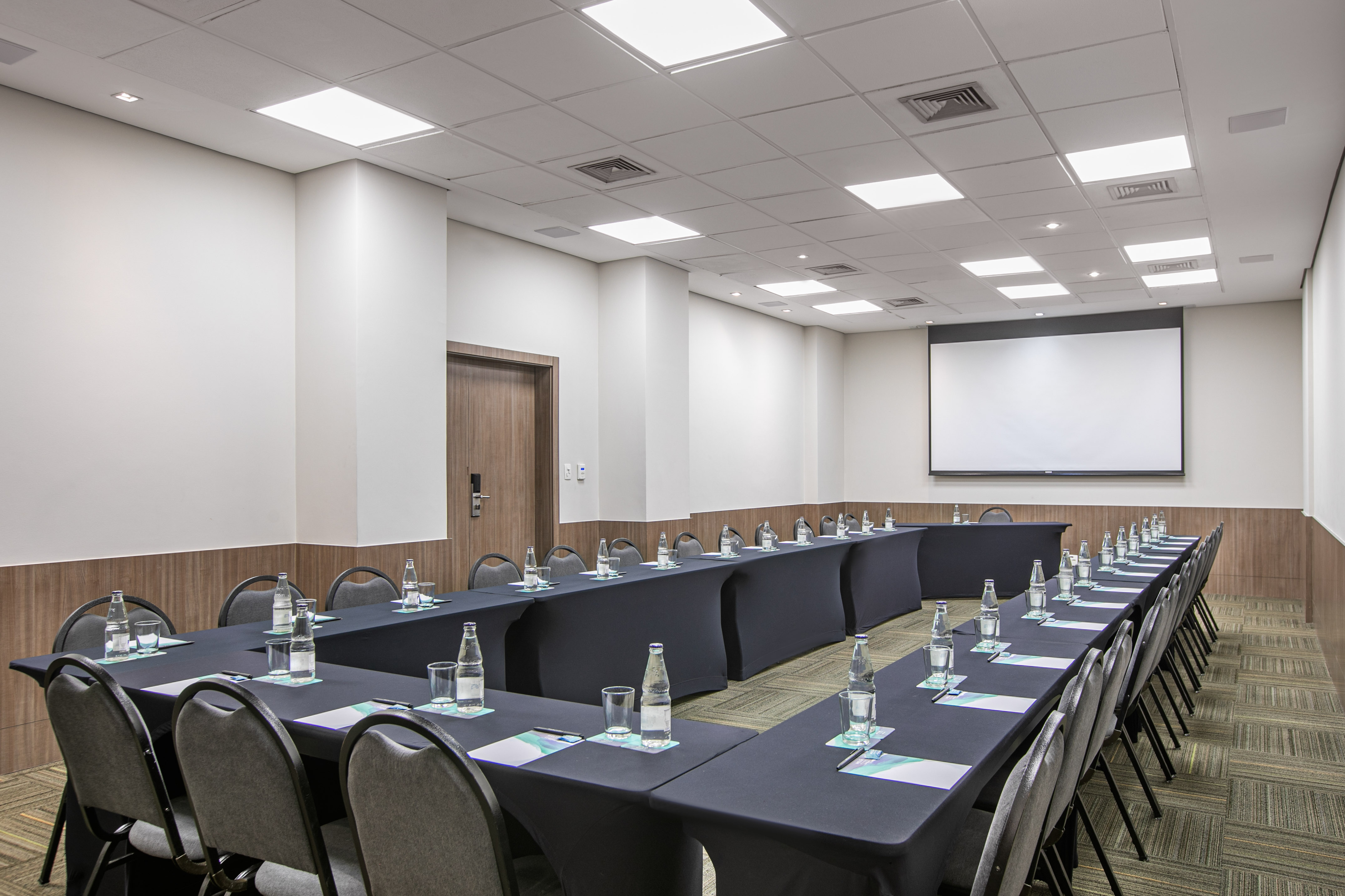 Modern U-shaped conference room with black tables and projector screen.