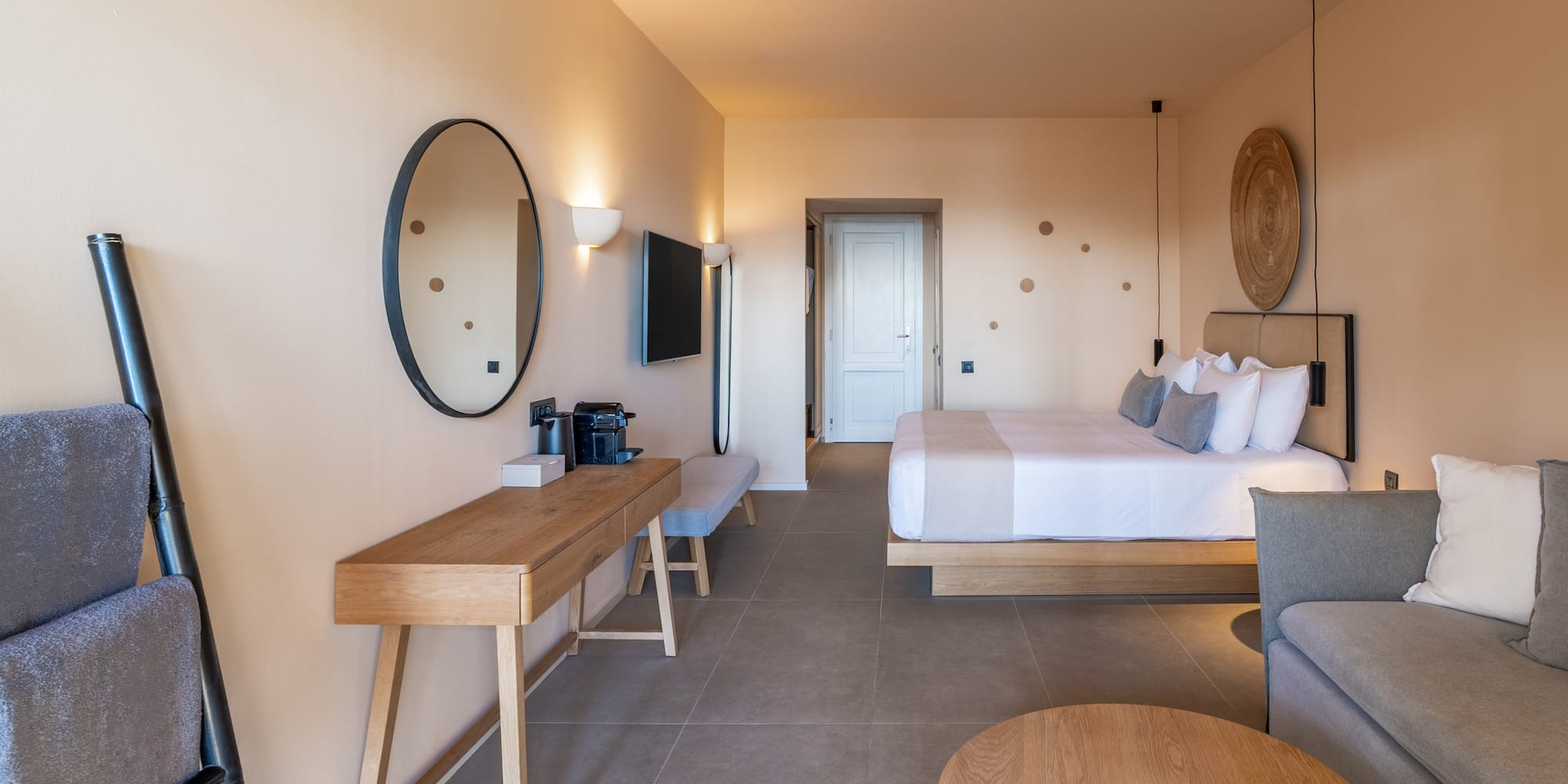 Luxury hotel room with king bed, neutral decor, sofa, and wooden vanity.