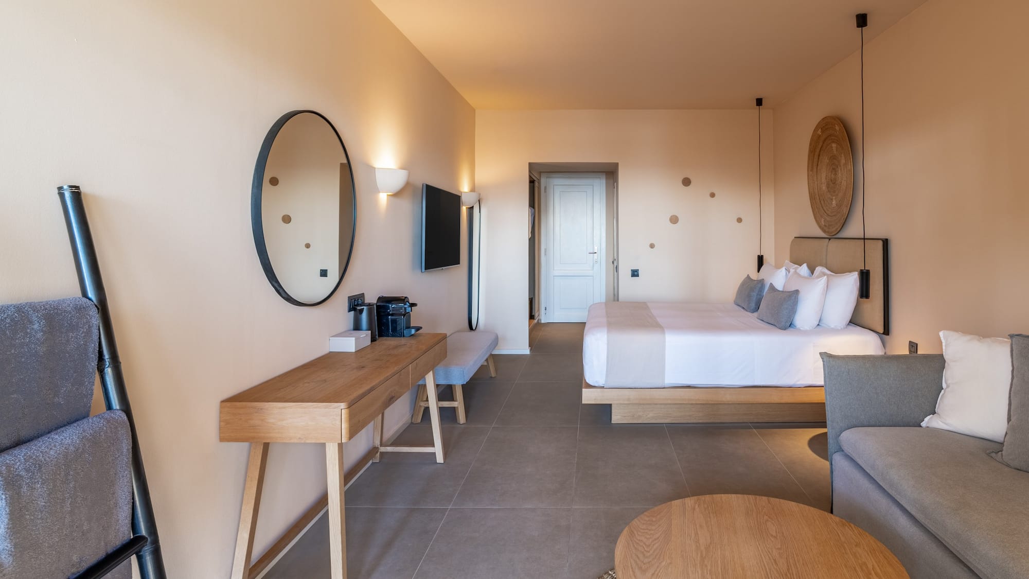 Luxury hotel room with king bed, neutral decor, sofa, and wooden vanity.