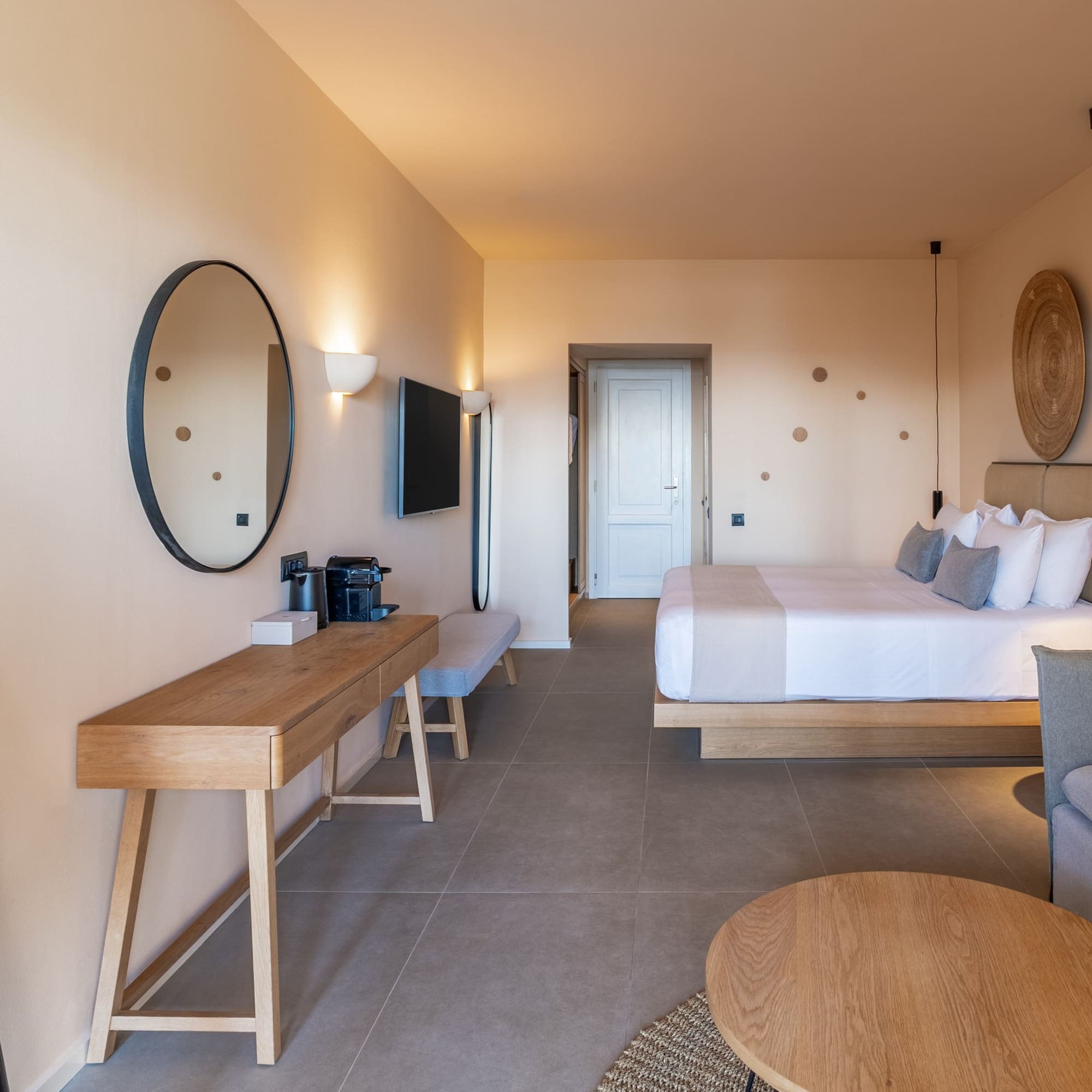 Luxury hotel room with king bed, neutral decor, sofa, and wooden vanity.
