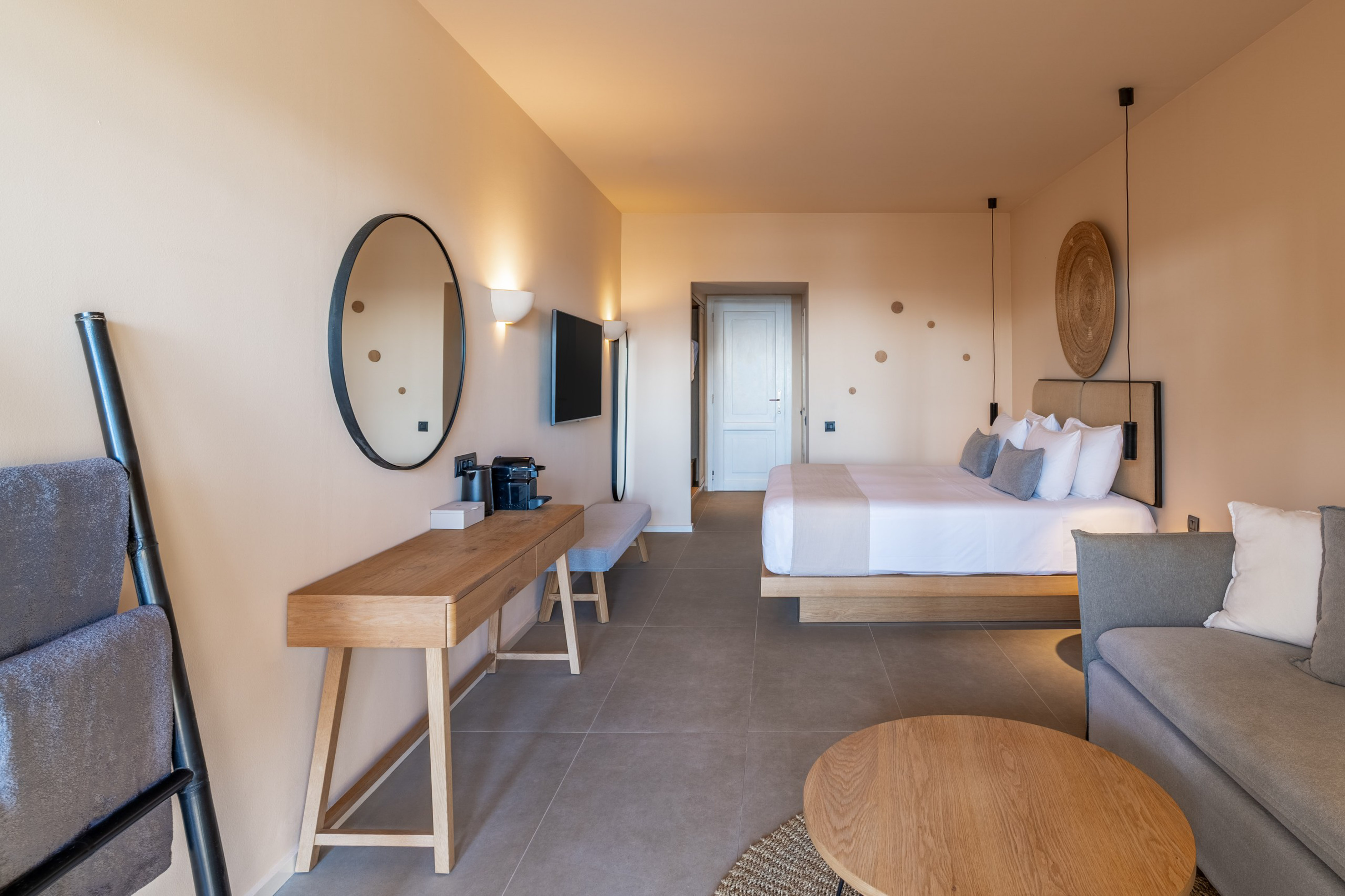 Luxury hotel room with king bed, neutral decor, sofa, and wooden vanity.