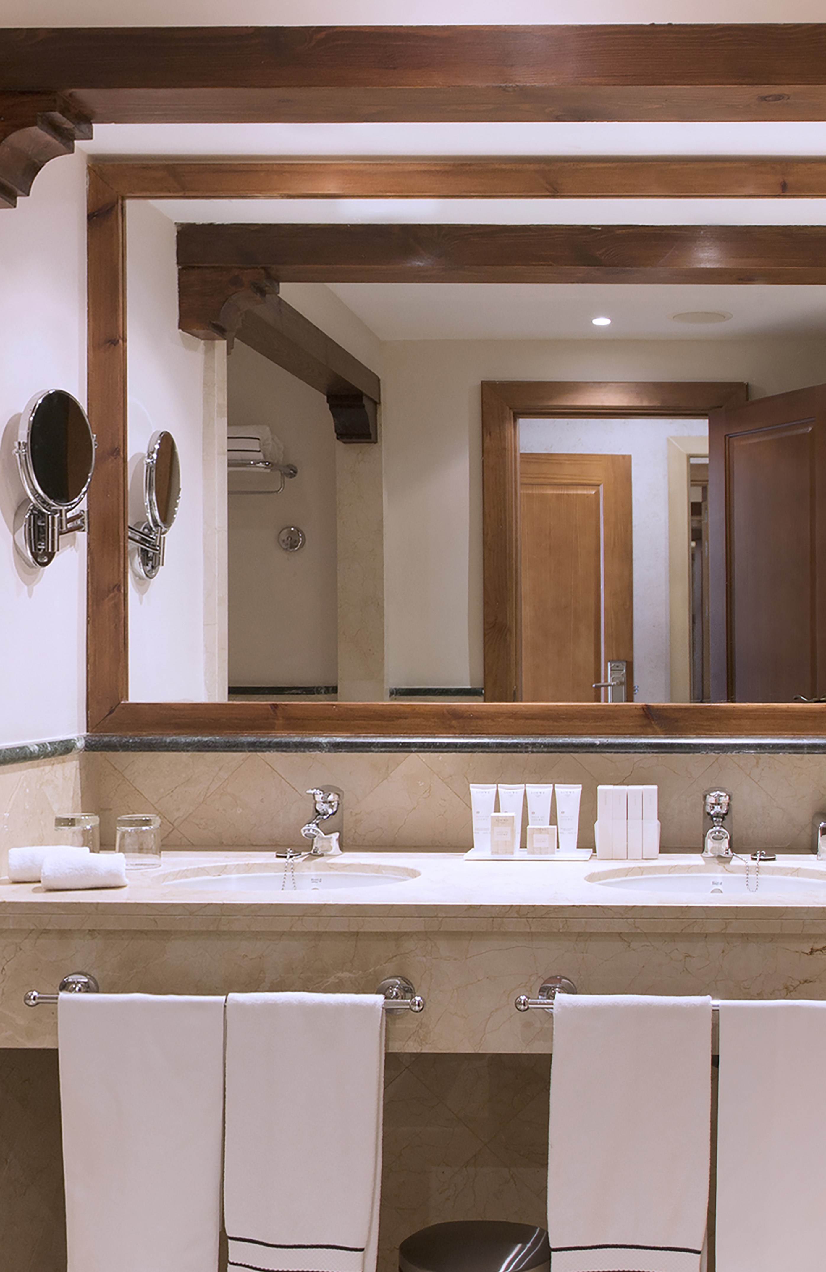 Hotel bathroom double vanity with marble top, wood mirror, and white towels.