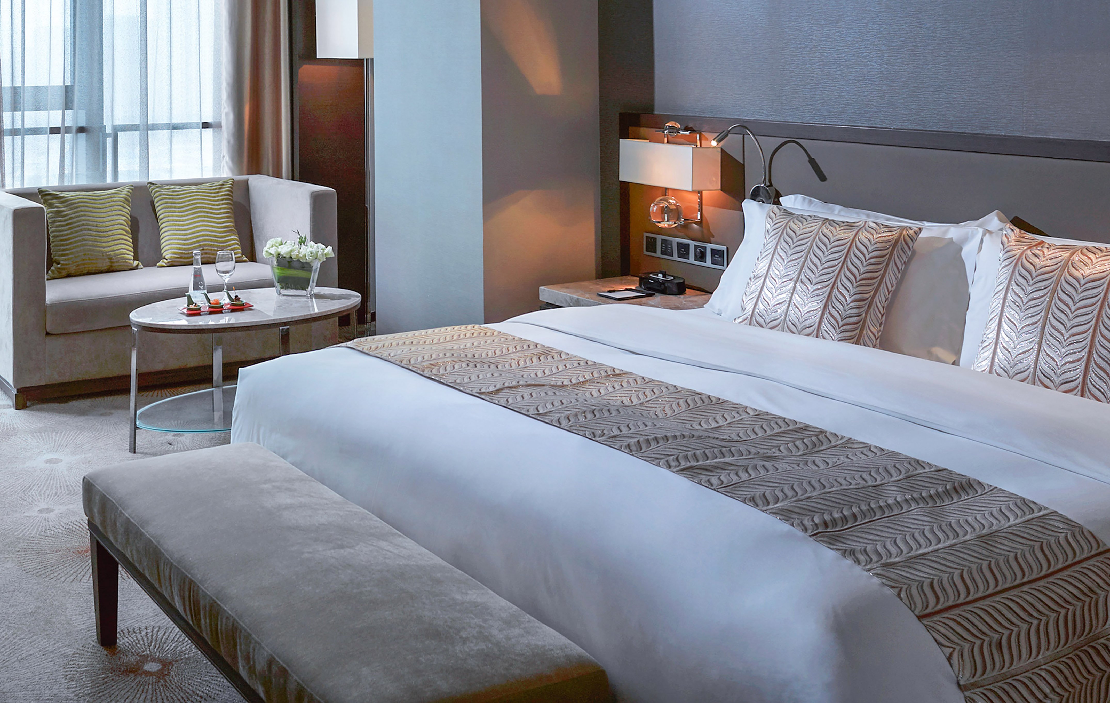 Modern hotel room with king bed, patterned runner, sofa, and coffee table.