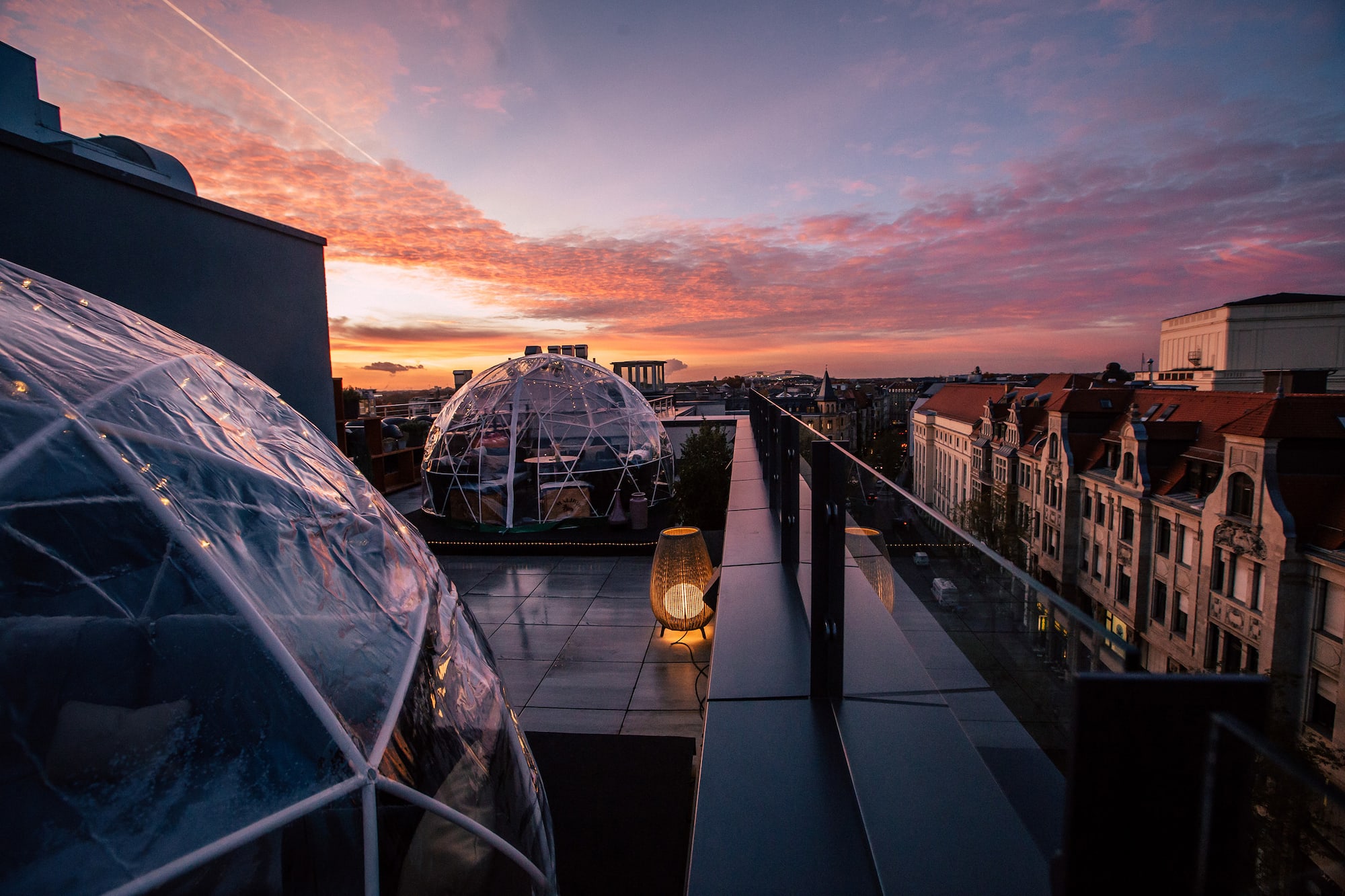 Rooftop terrace with igloo domes and city skyline under a vibrant sunset.