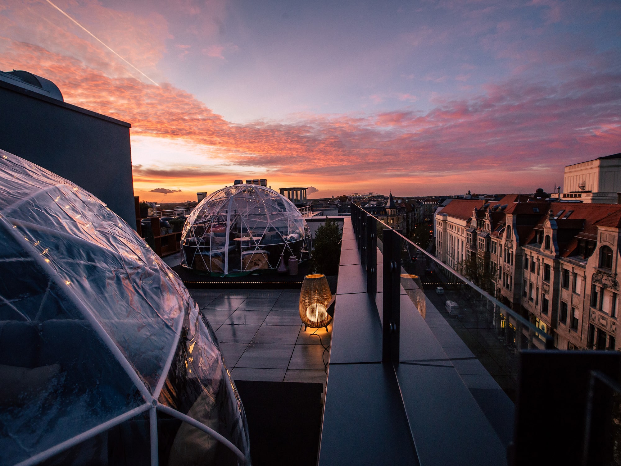 Rooftop terrace with igloo domes and city skyline under a vibrant sunset.