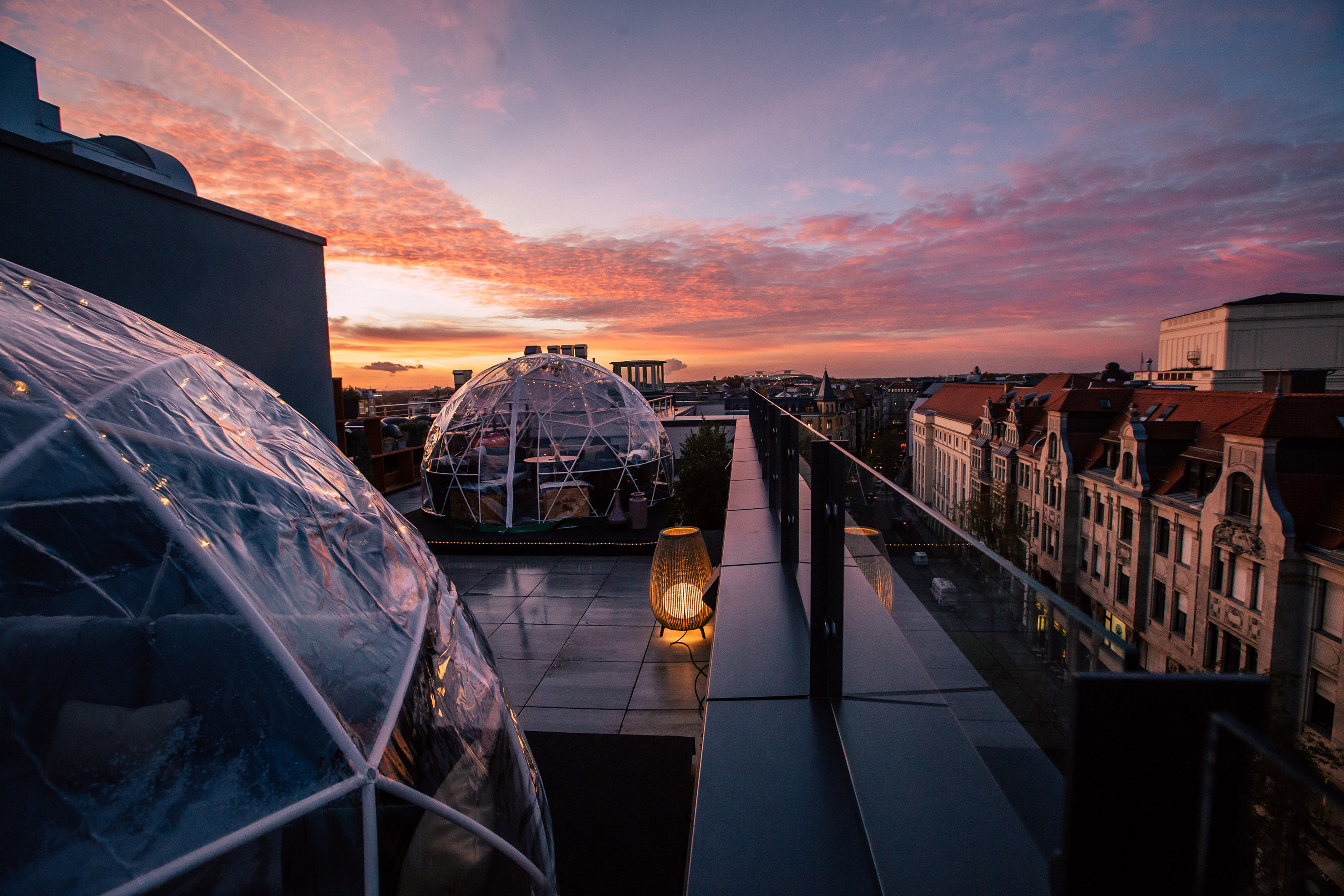 Rooftop terrace with igloo domes and city skyline under a vibrant sunset.