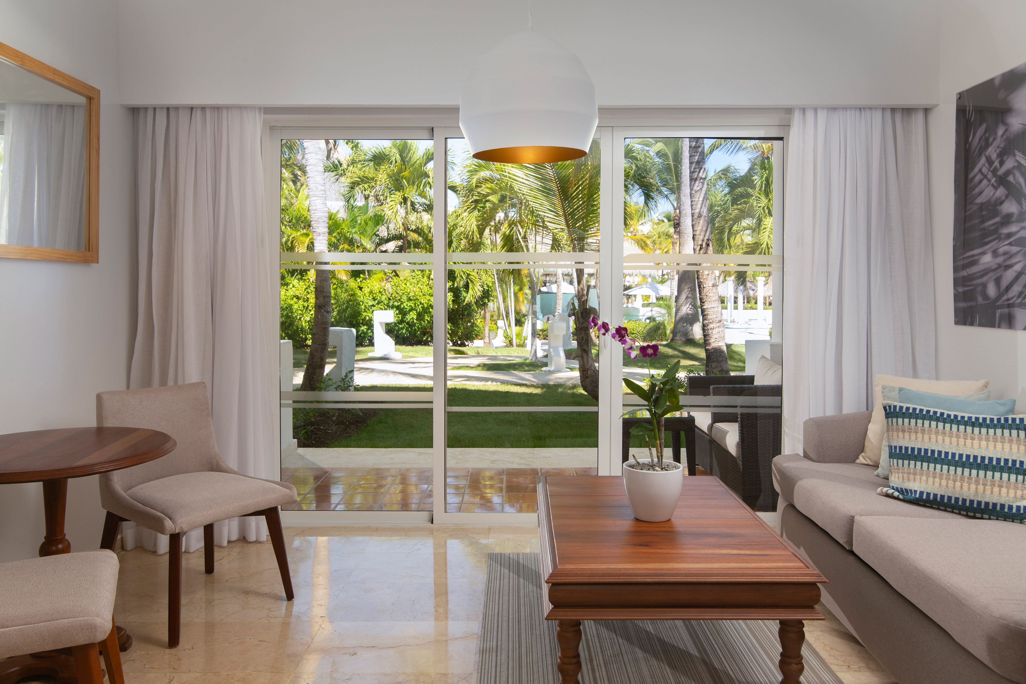Resort suite living room with tropical garden view and palm trees.