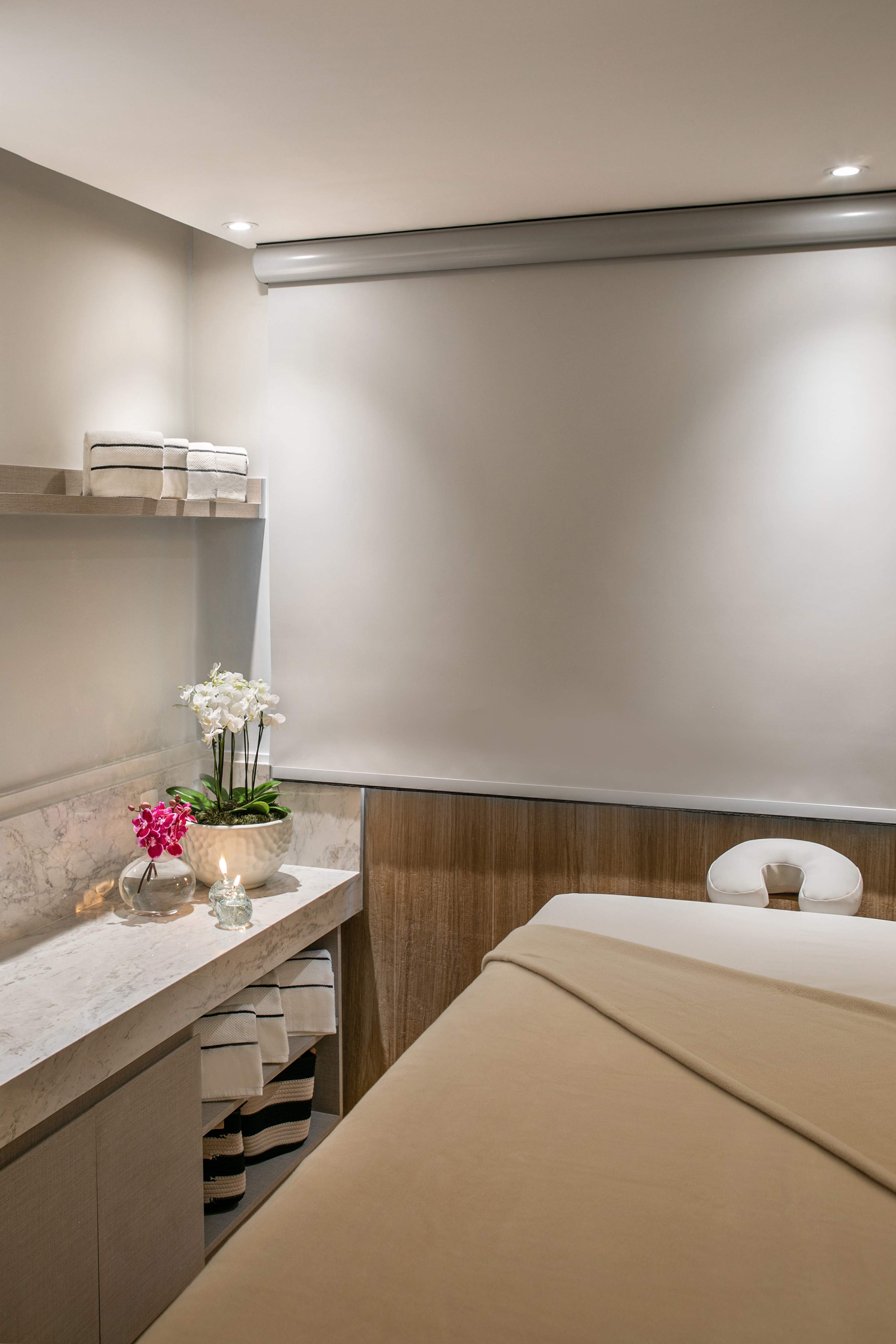 Spa treatment room with massage bed, white orchids, lit candle, and towels.