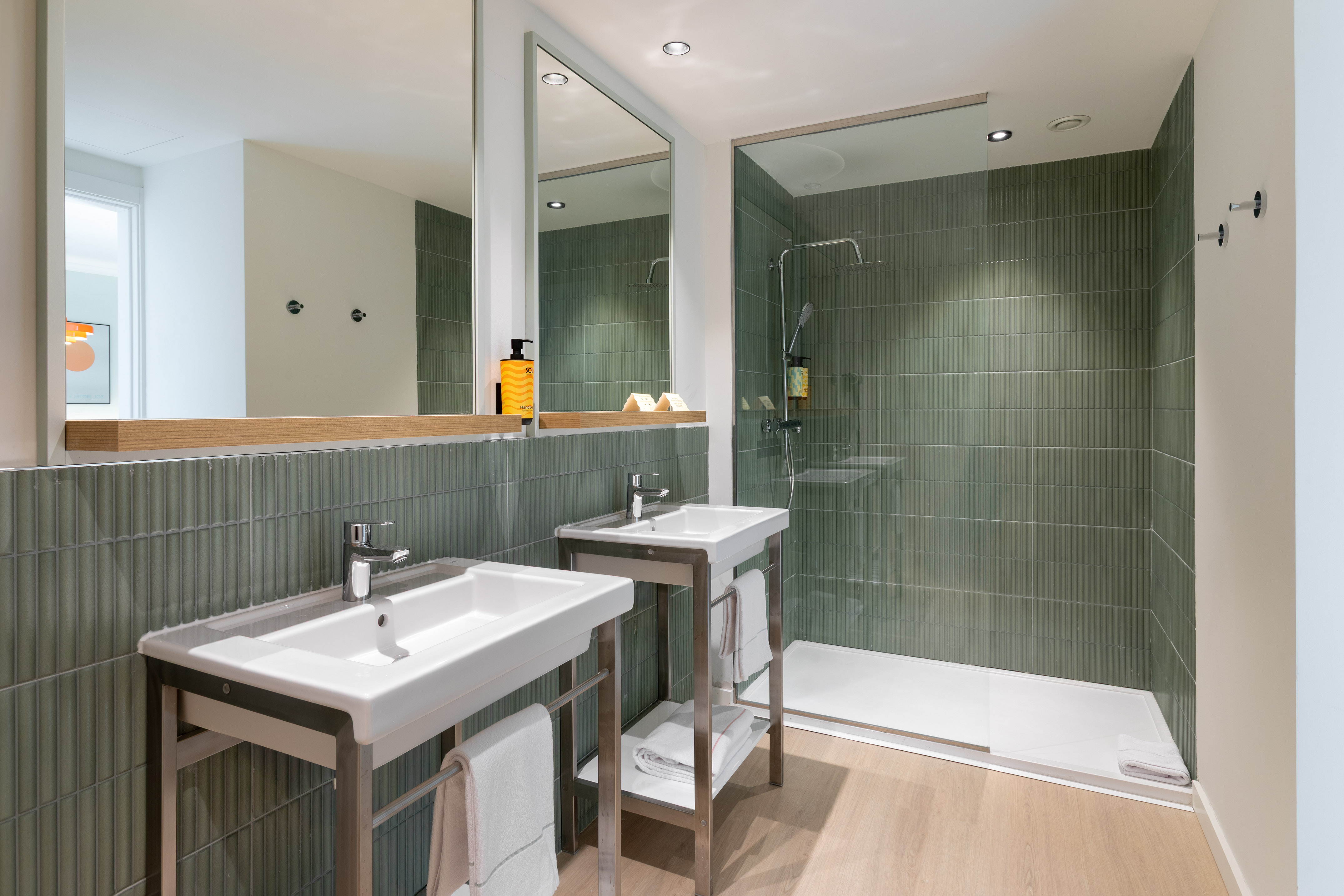 Contemporary hotel bathroom with dual sinks, green vertical tiles, and glass shower.