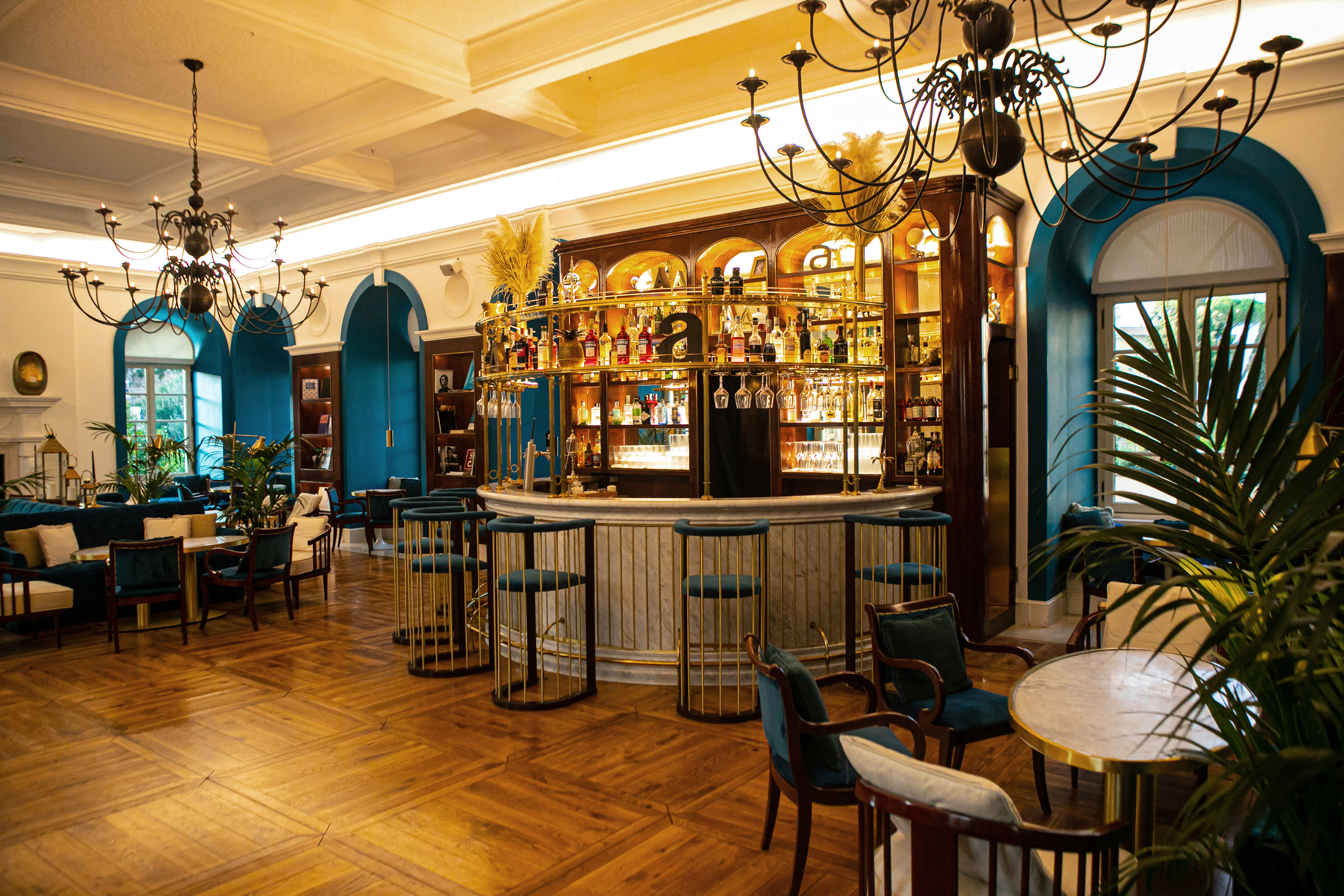 Elegant hotel bar with round brass bar, teal stools, and wood parquet floor.