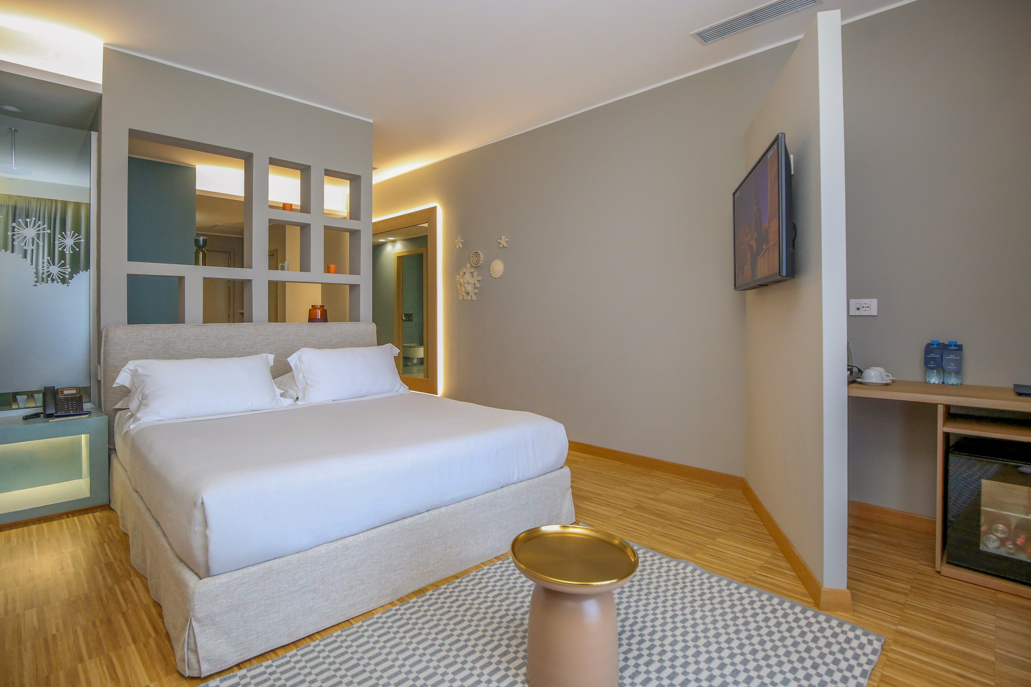 Modern hotel room with queen bed, wood floor, TV, and decorative wall panel.