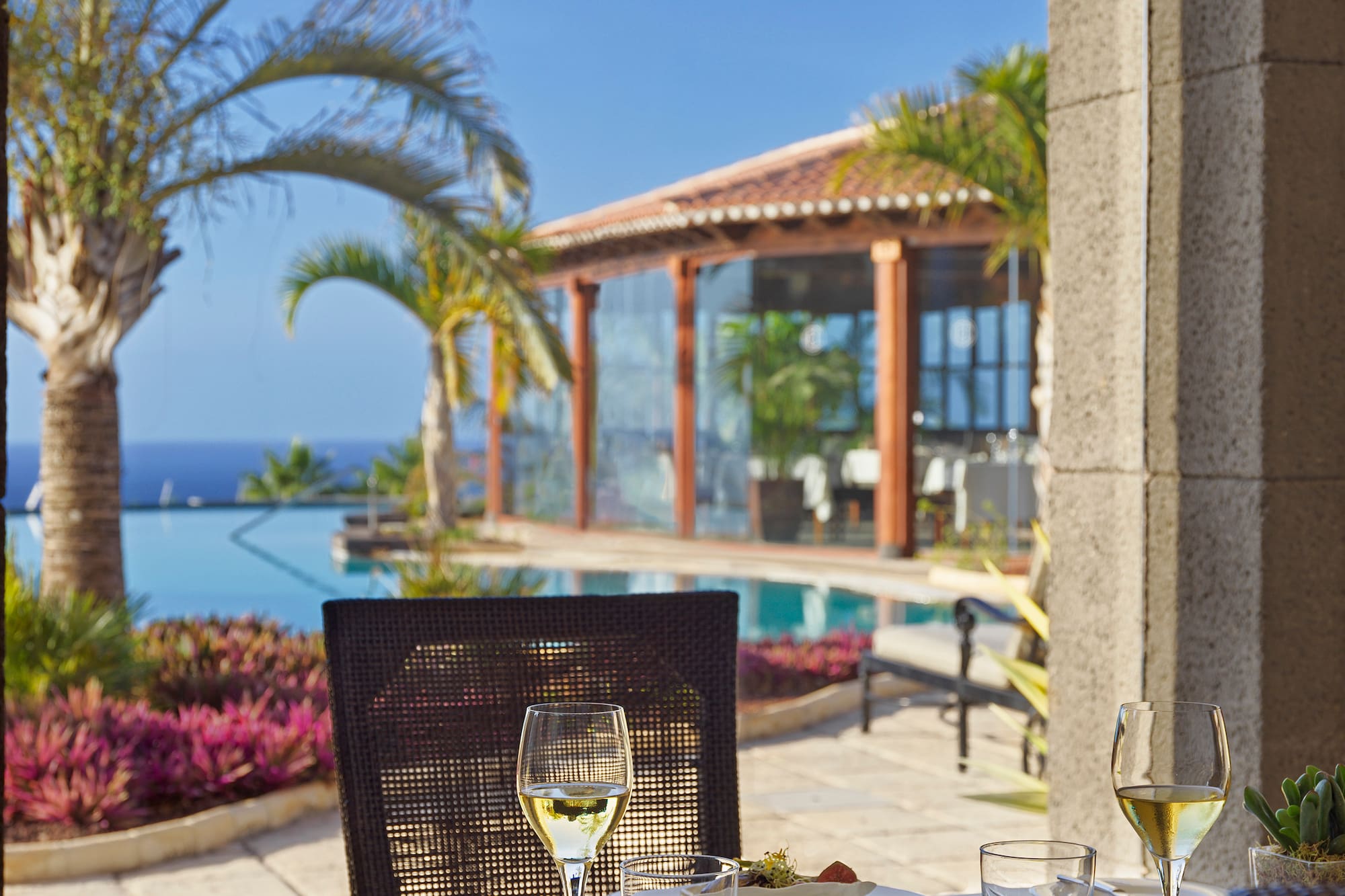 Luxury resort outdoor dining table with wine, ocean view, and infinity pool.