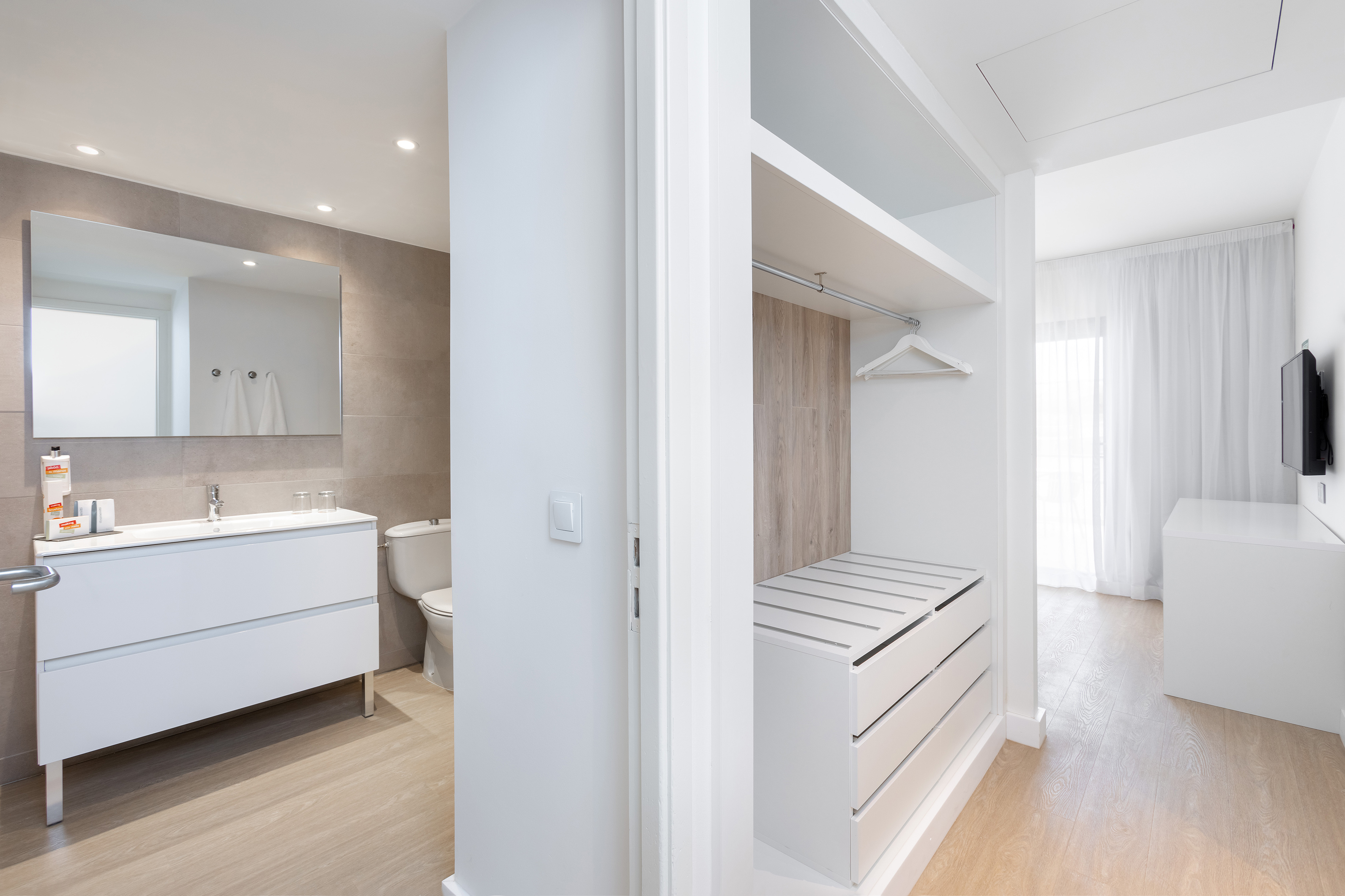 Bright modern hotel bathroom and open closet with light wood floor.