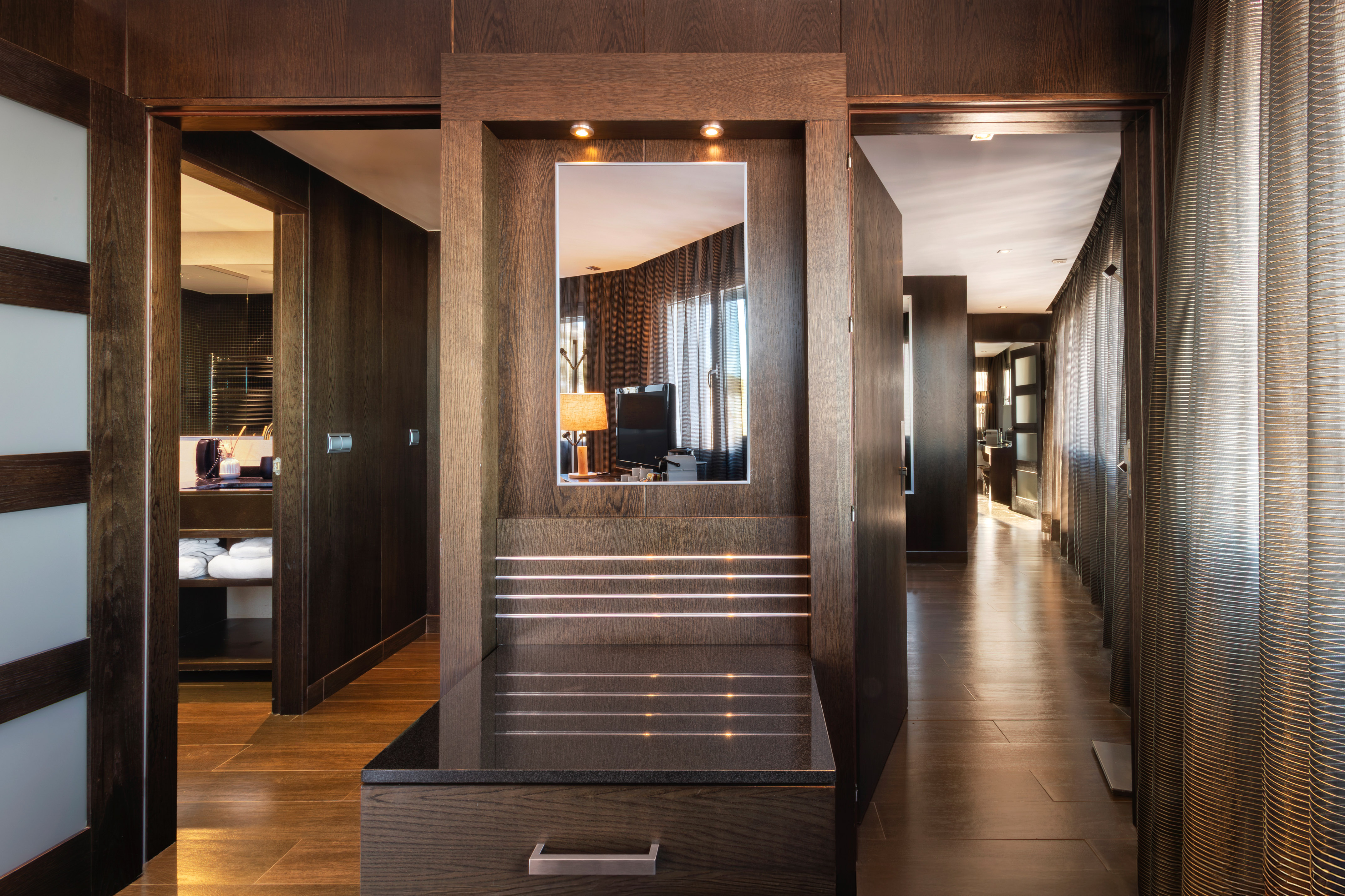 Luxury hotel entryway with dark wood paneling, lit mirror, and hallway.