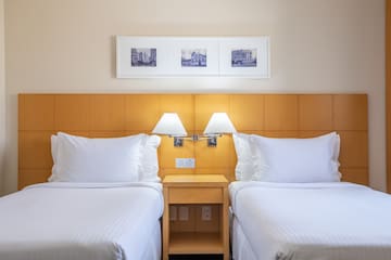 two beds with white sheets and lamps in a hotel room