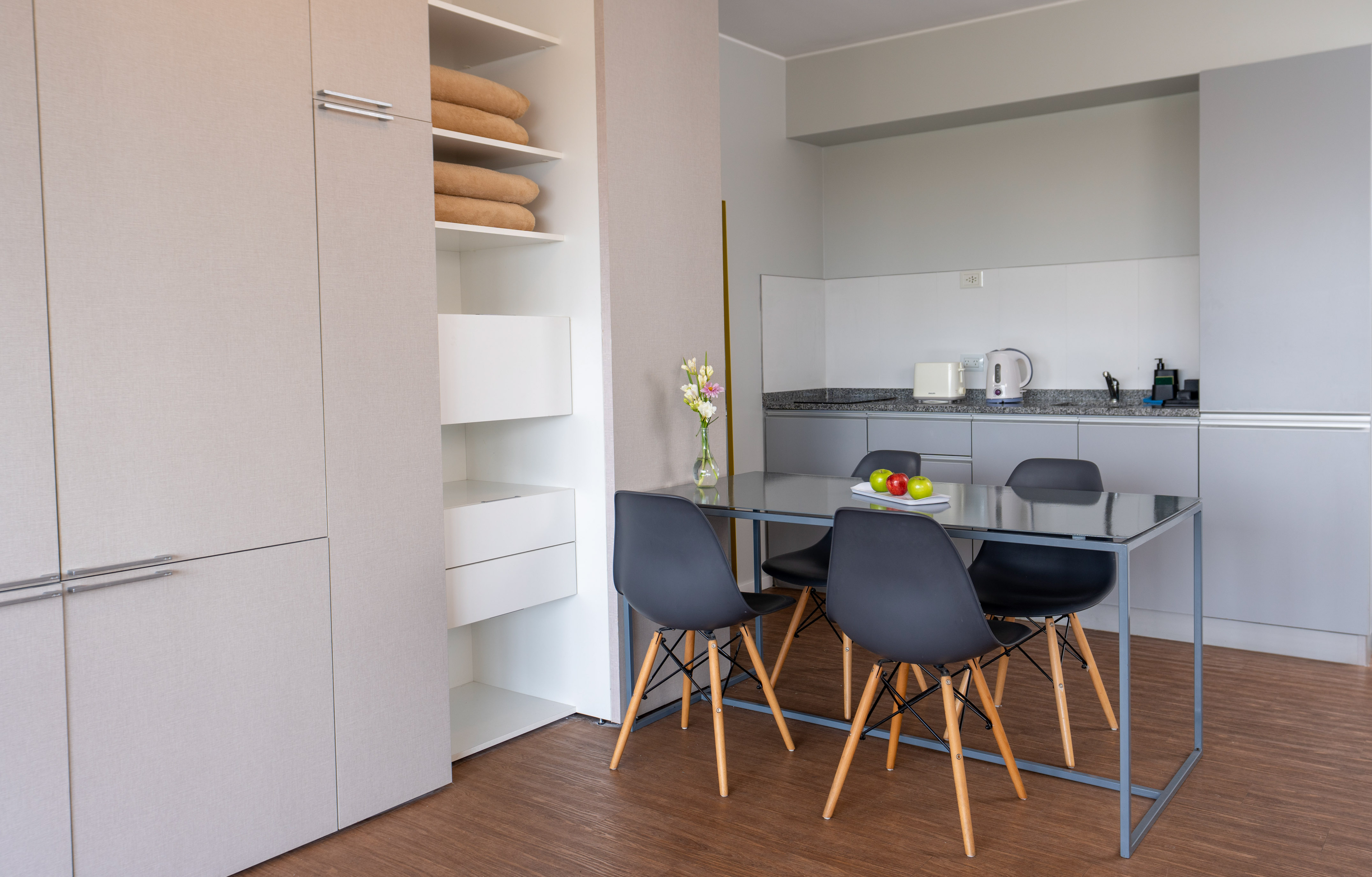 Modern kitchen and dining area with grey cabinets, glass table, black chairs.