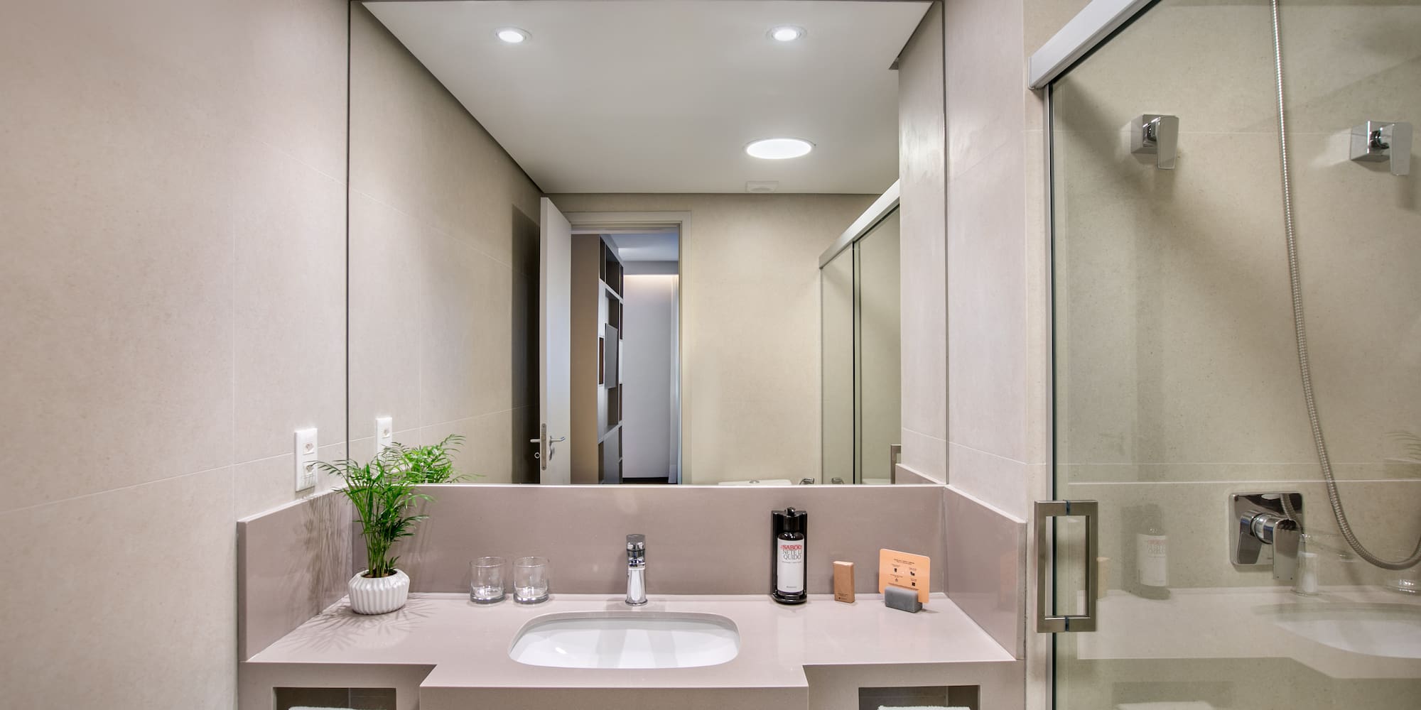 Modern hotel bathroom with sleek vanity, sink, mirror, and glass shower.