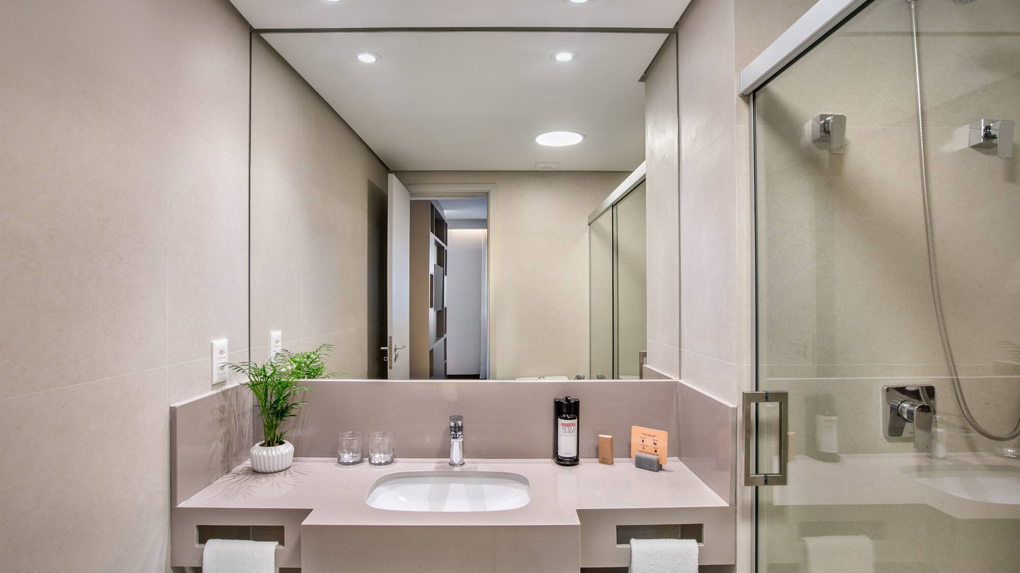 Modern hotel bathroom with sleek vanity, sink, mirror, and glass shower.