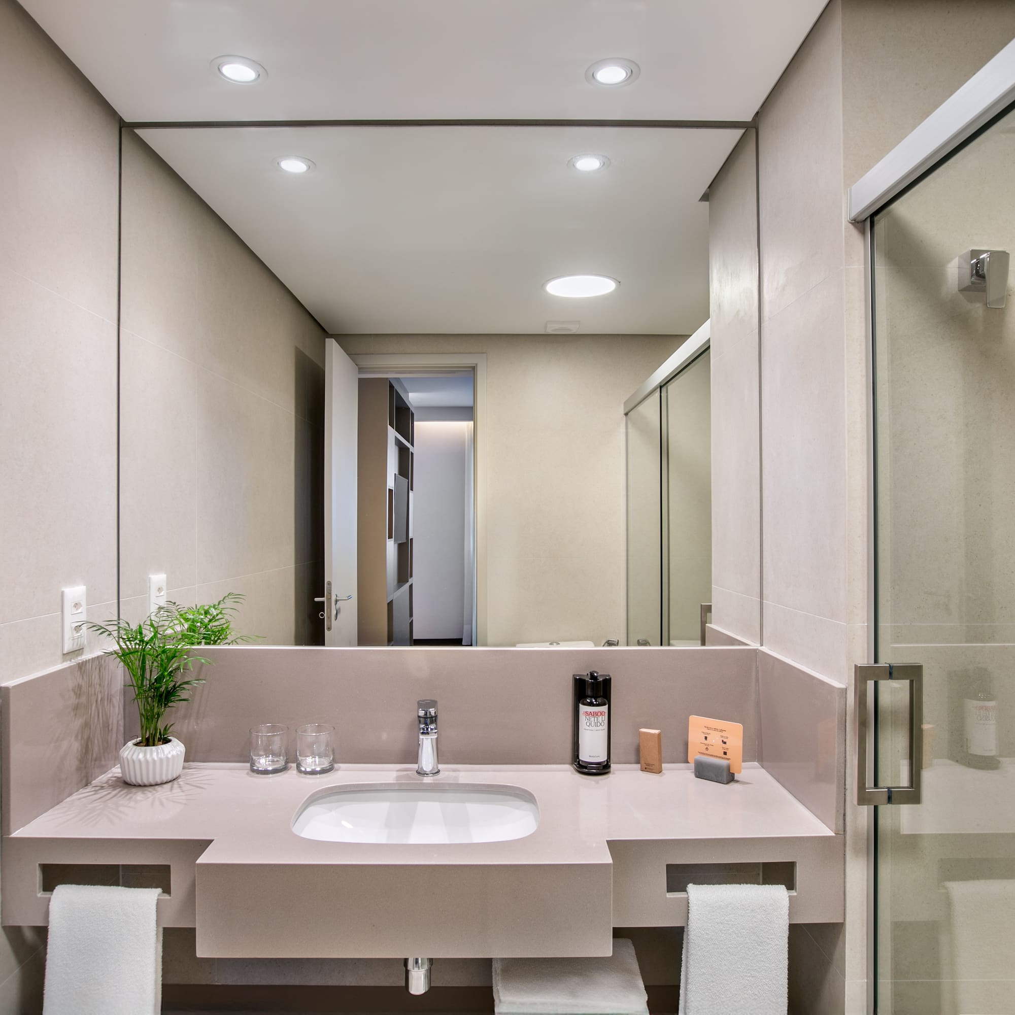 Modern hotel bathroom with sleek vanity, sink, mirror, and glass shower.