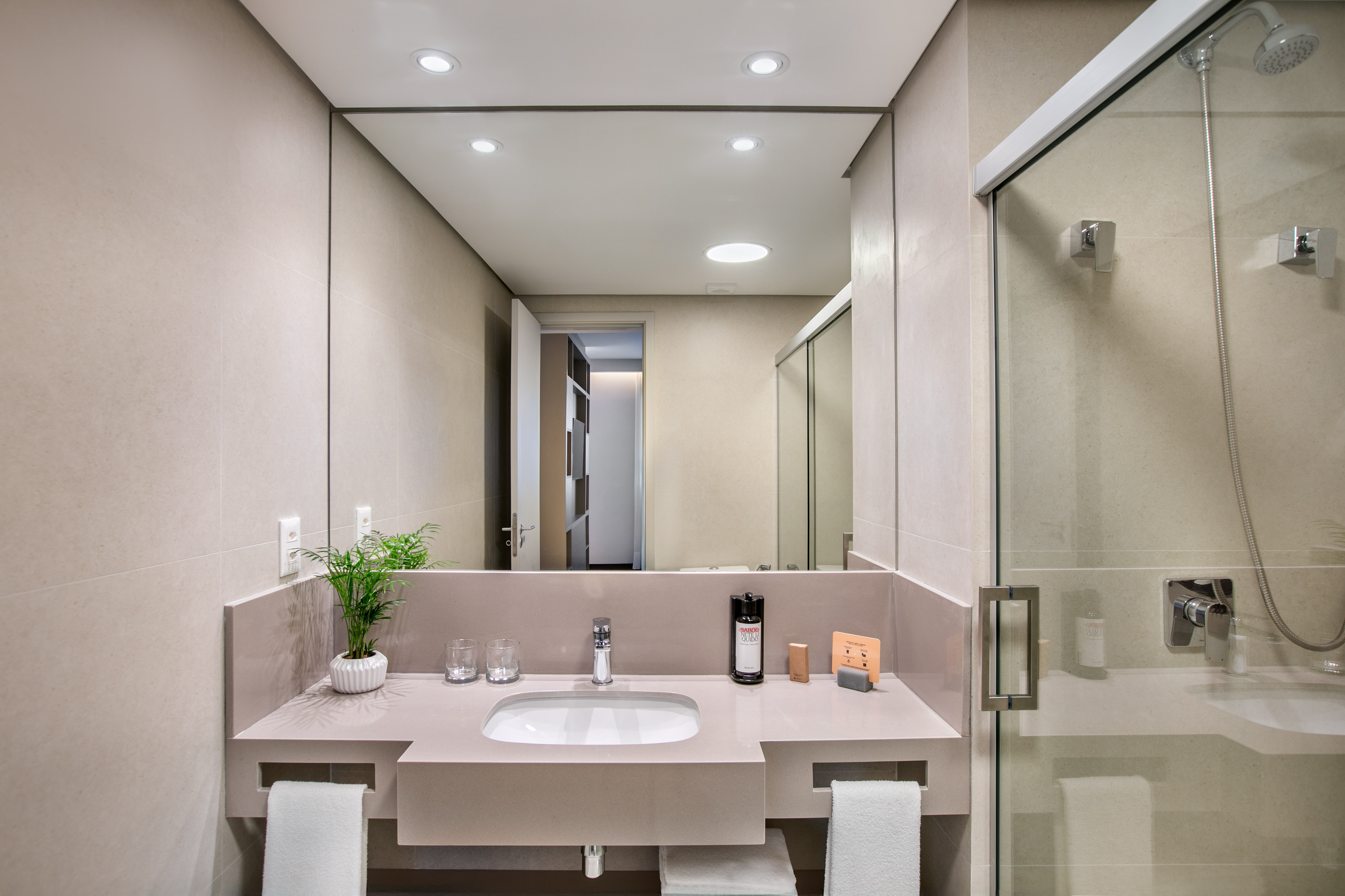 Modern hotel bathroom with sleek vanity, sink, mirror, and glass shower.
