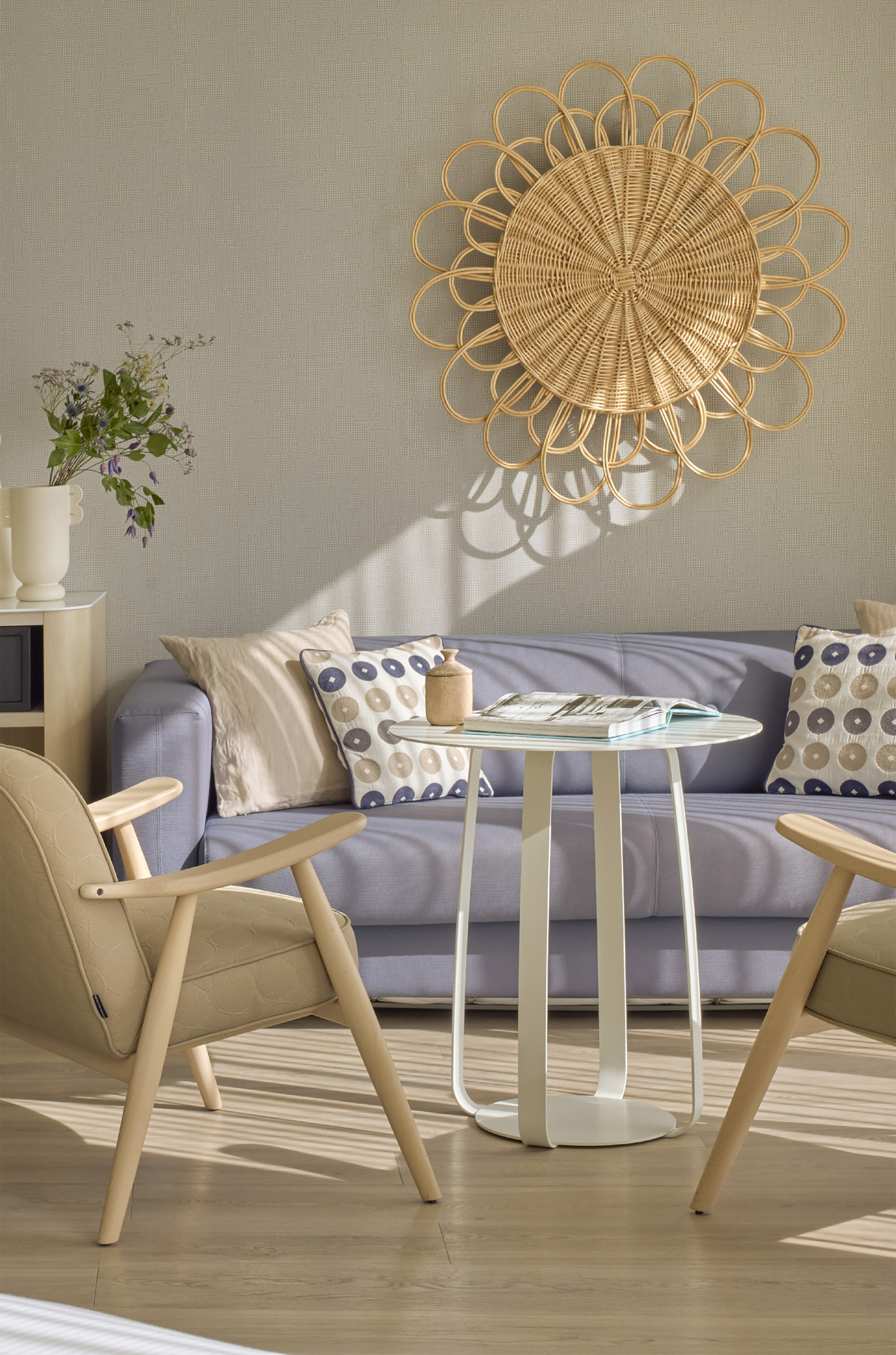 Modern living room: blue sofa, beige chair, white table, rattan sunburst wall art.