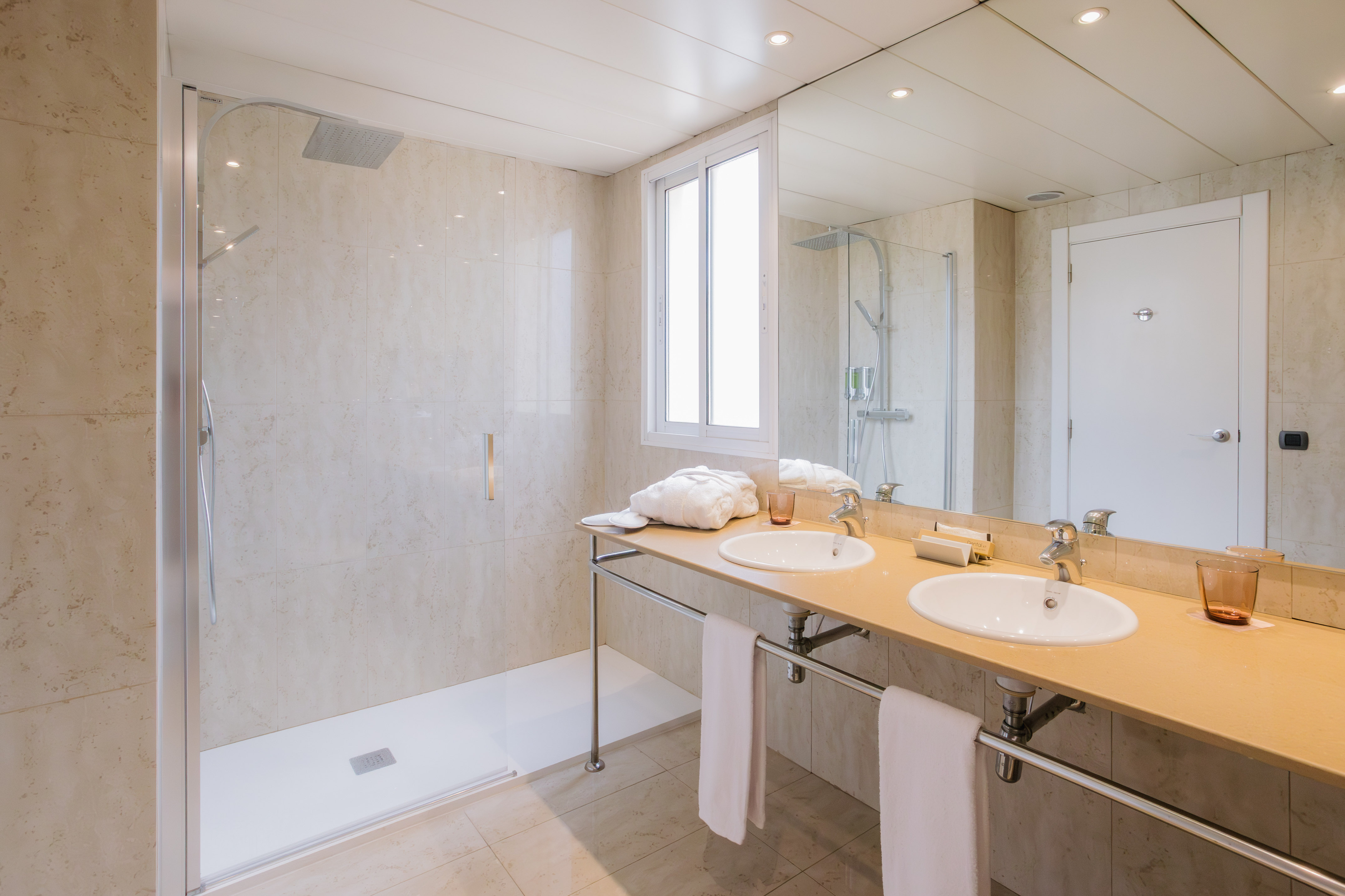 Modern bathroom with walk-in shower, double vanity, large mirror, and window.