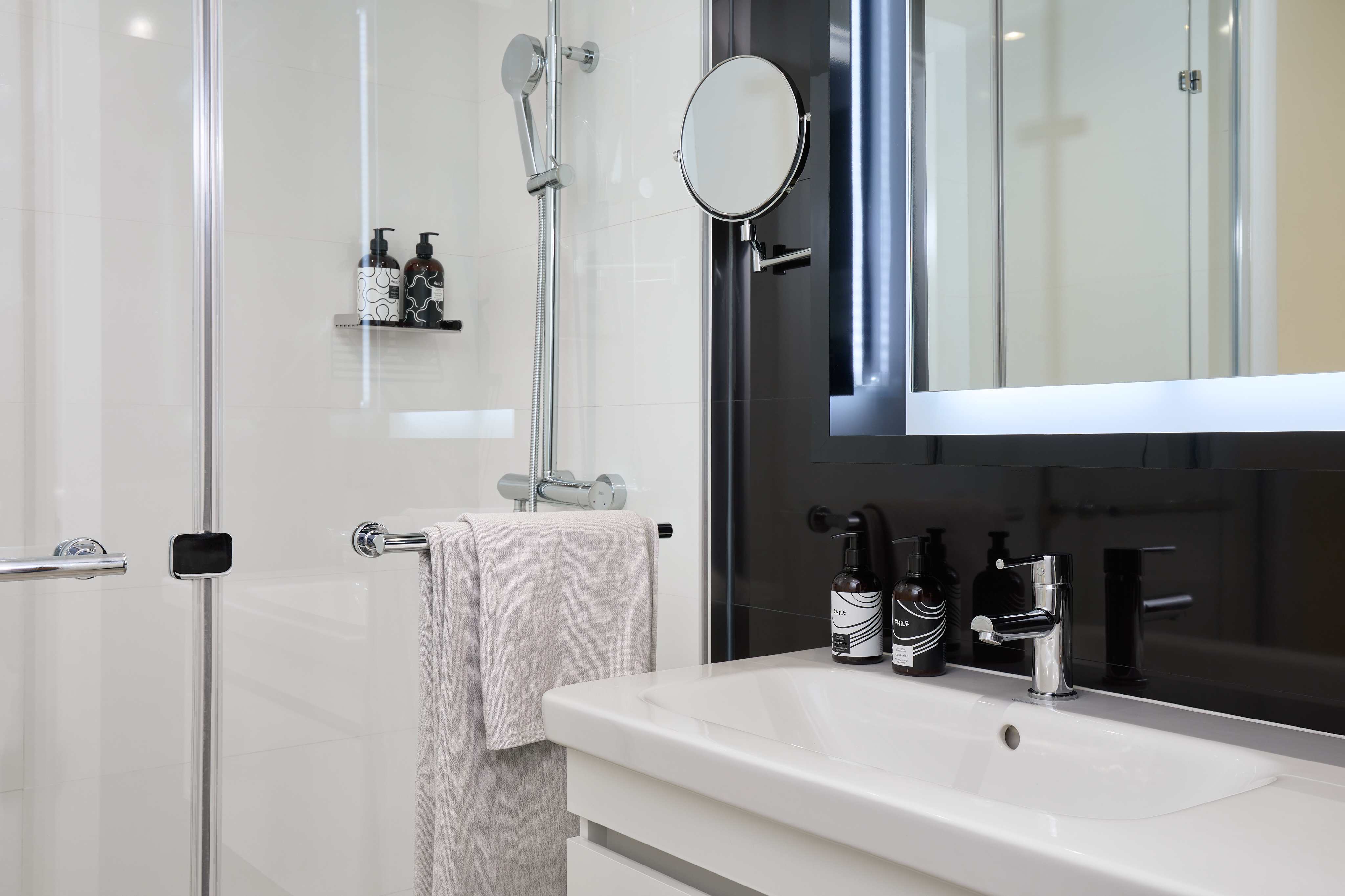 Modern white bathroom with glass shower, vanity sink, and illuminated mirror.