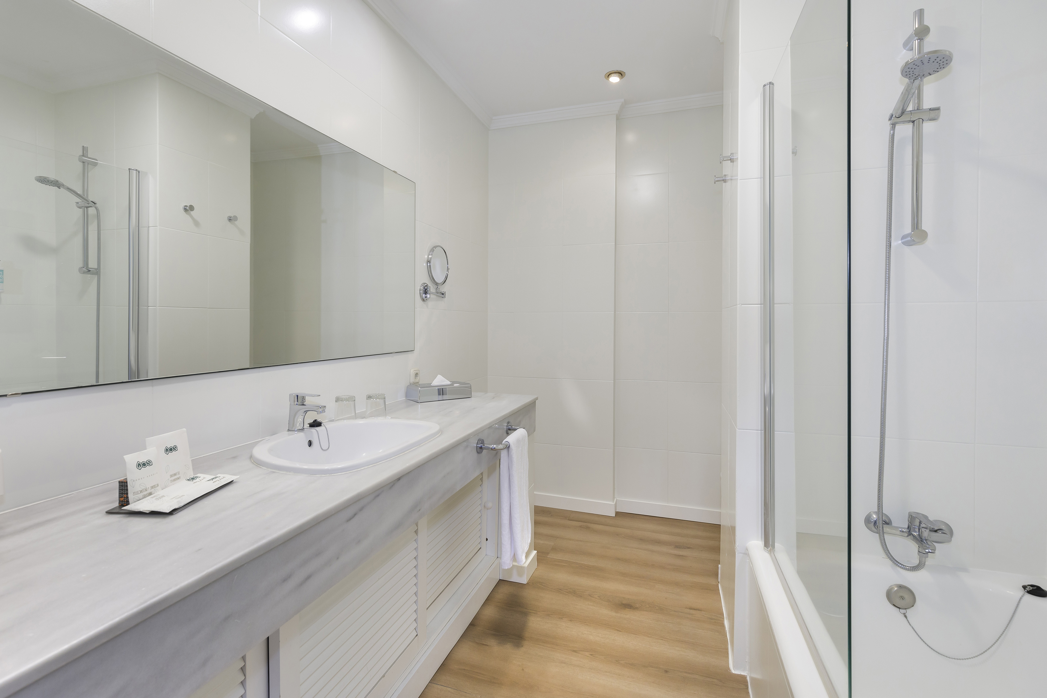White hotel bathroom with marble vanity, sink, mirror, and shower-tub.