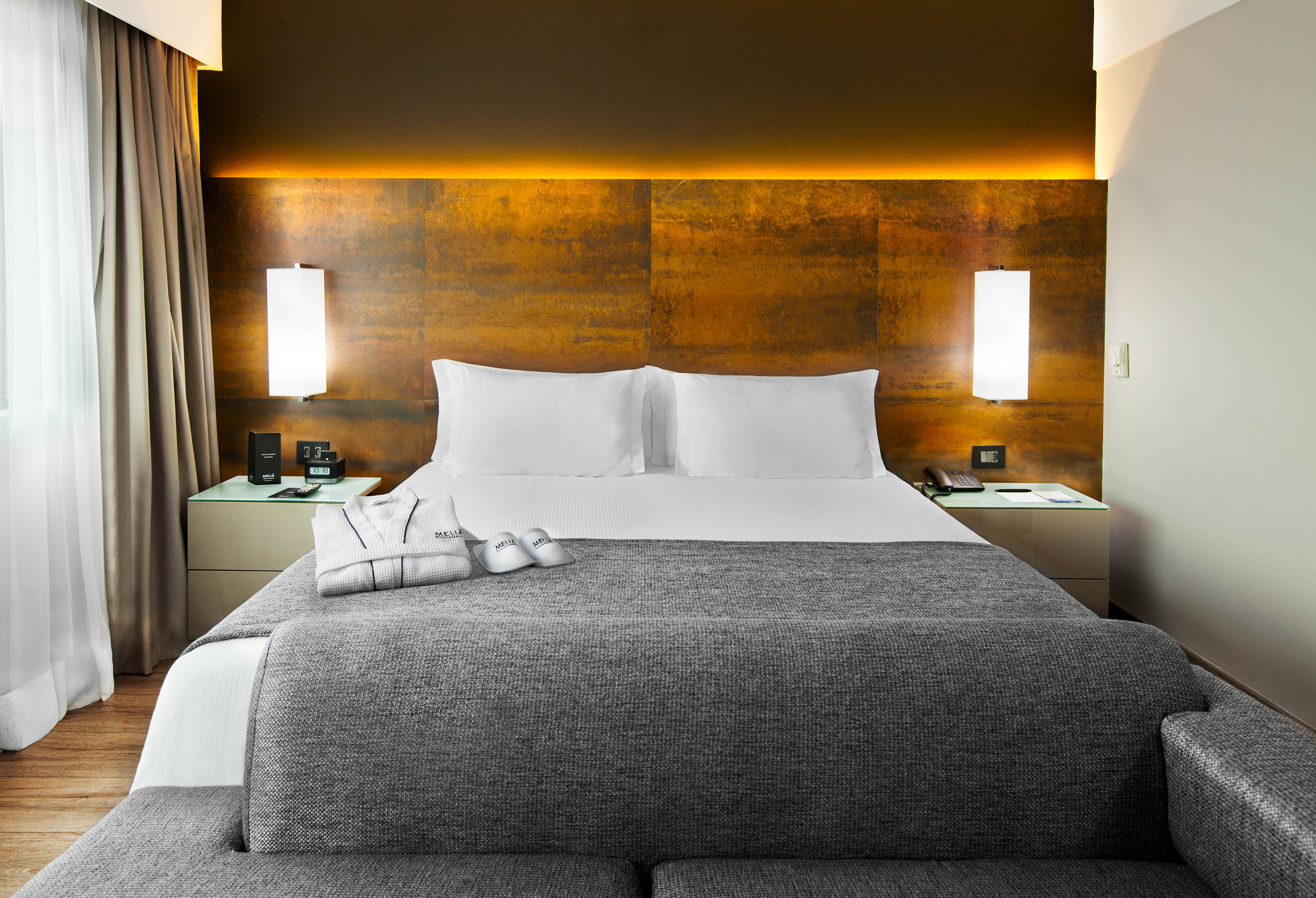 Modern Meliá hotel room with king bed, grey blanket, and illuminated headboard.