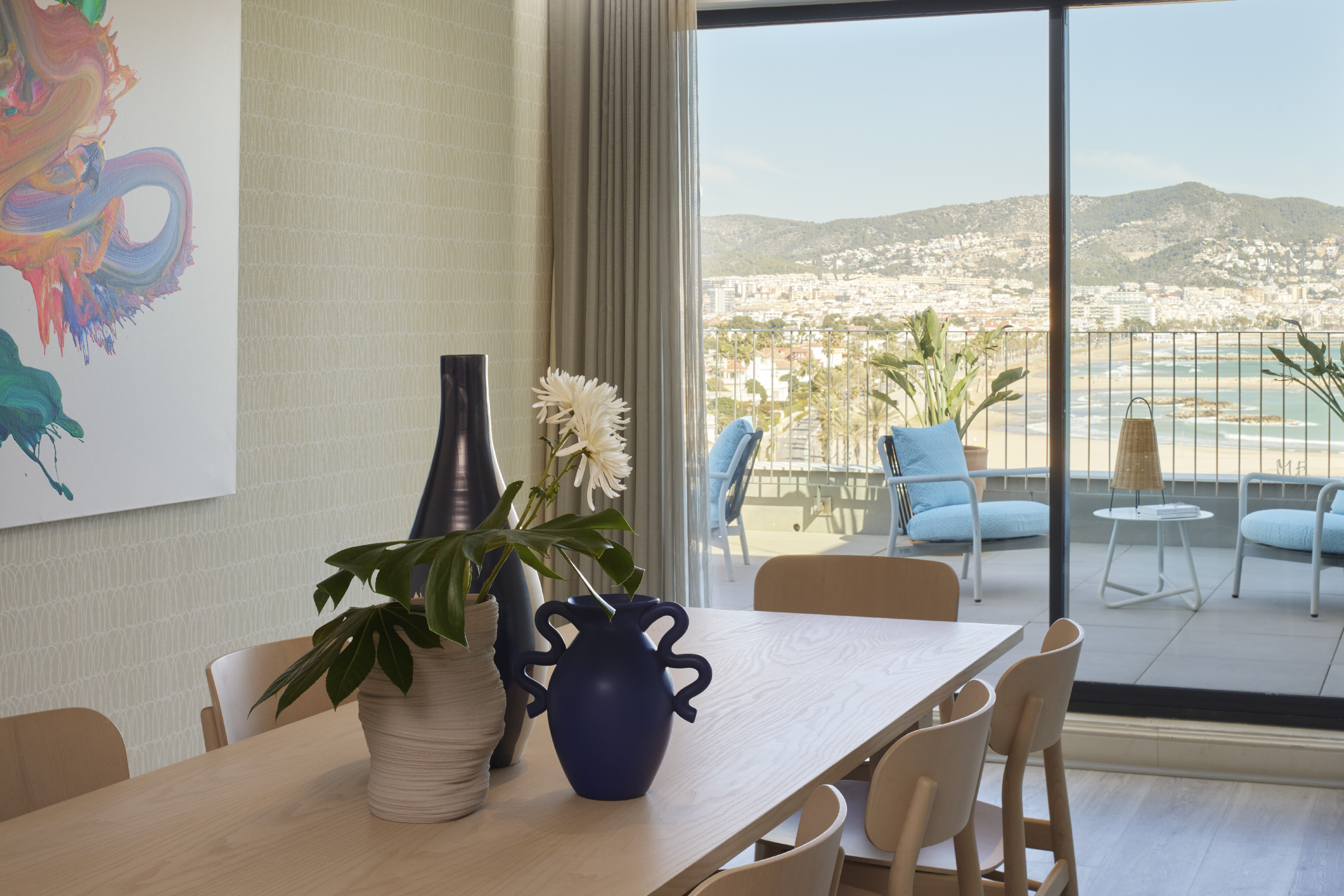 Modern dining room with balcony overlooking beach, city, and mountains.