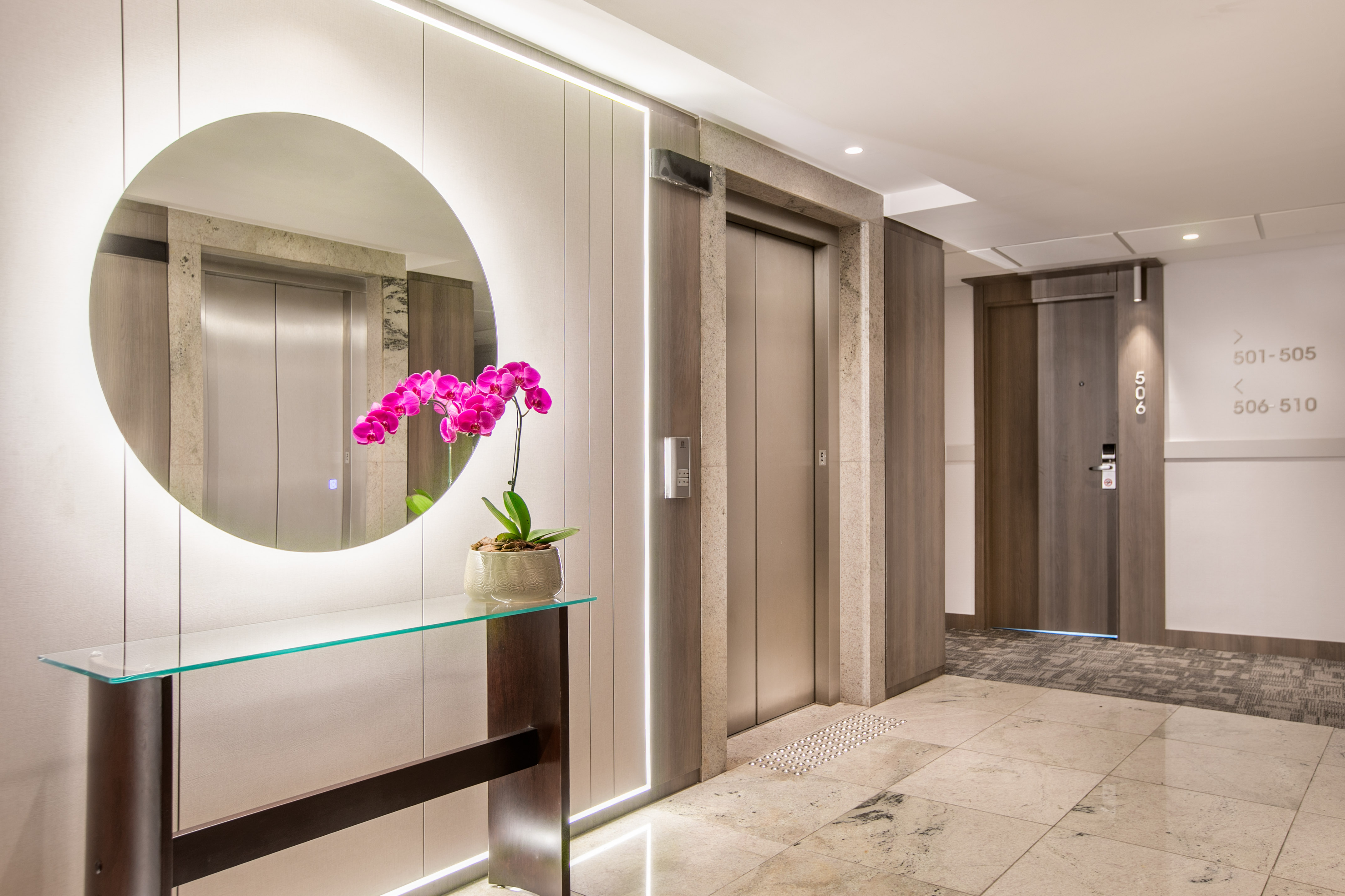 Modern hotel lobby, sleek elevators, illuminated mirror, pink orchid.