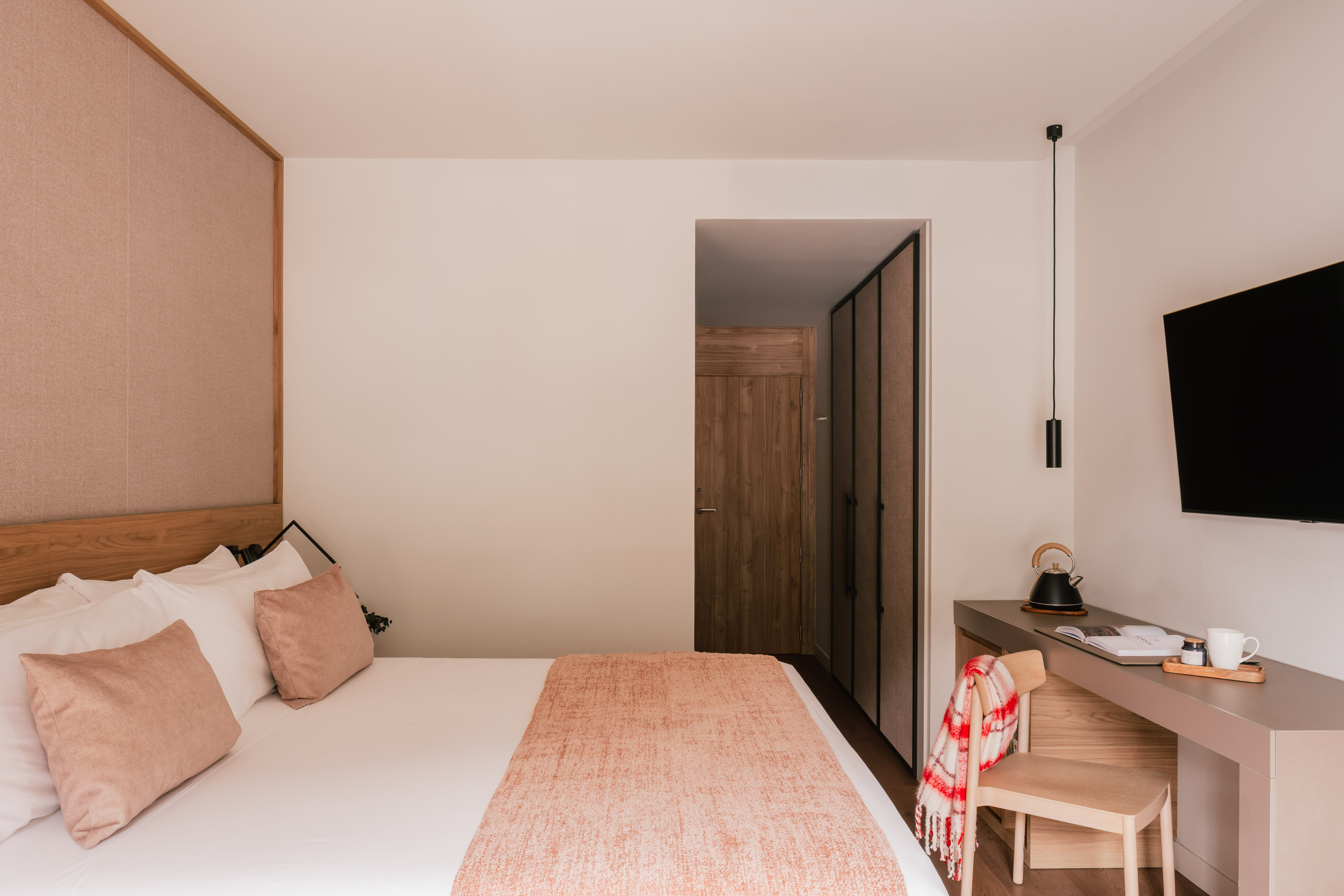 Modern hotel bedroom with cozy bed, wood headboard, desk, and flat-screen TV.