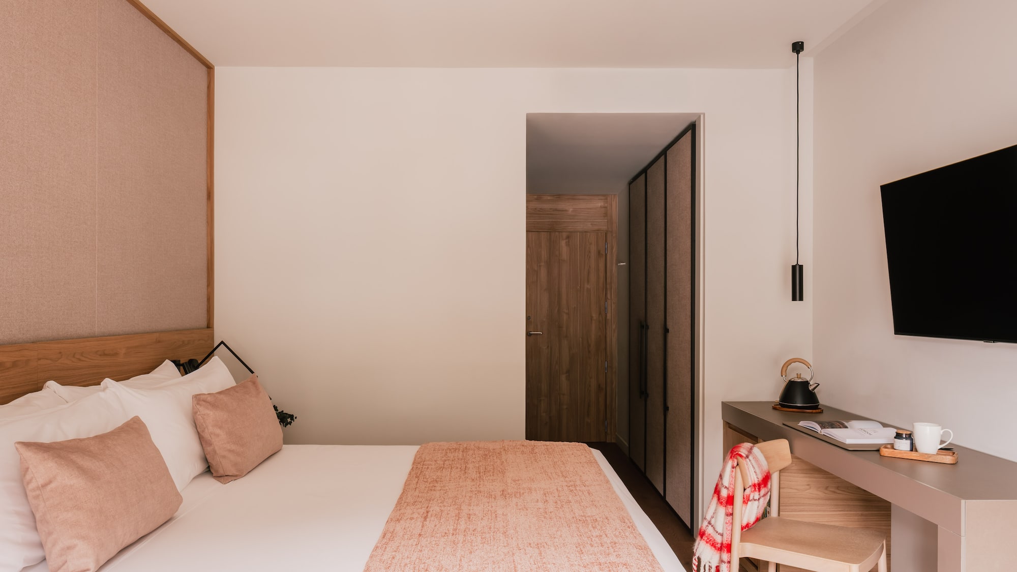 Modern hotel bedroom with cozy bed, wood headboard, desk, and flat-screen TV.