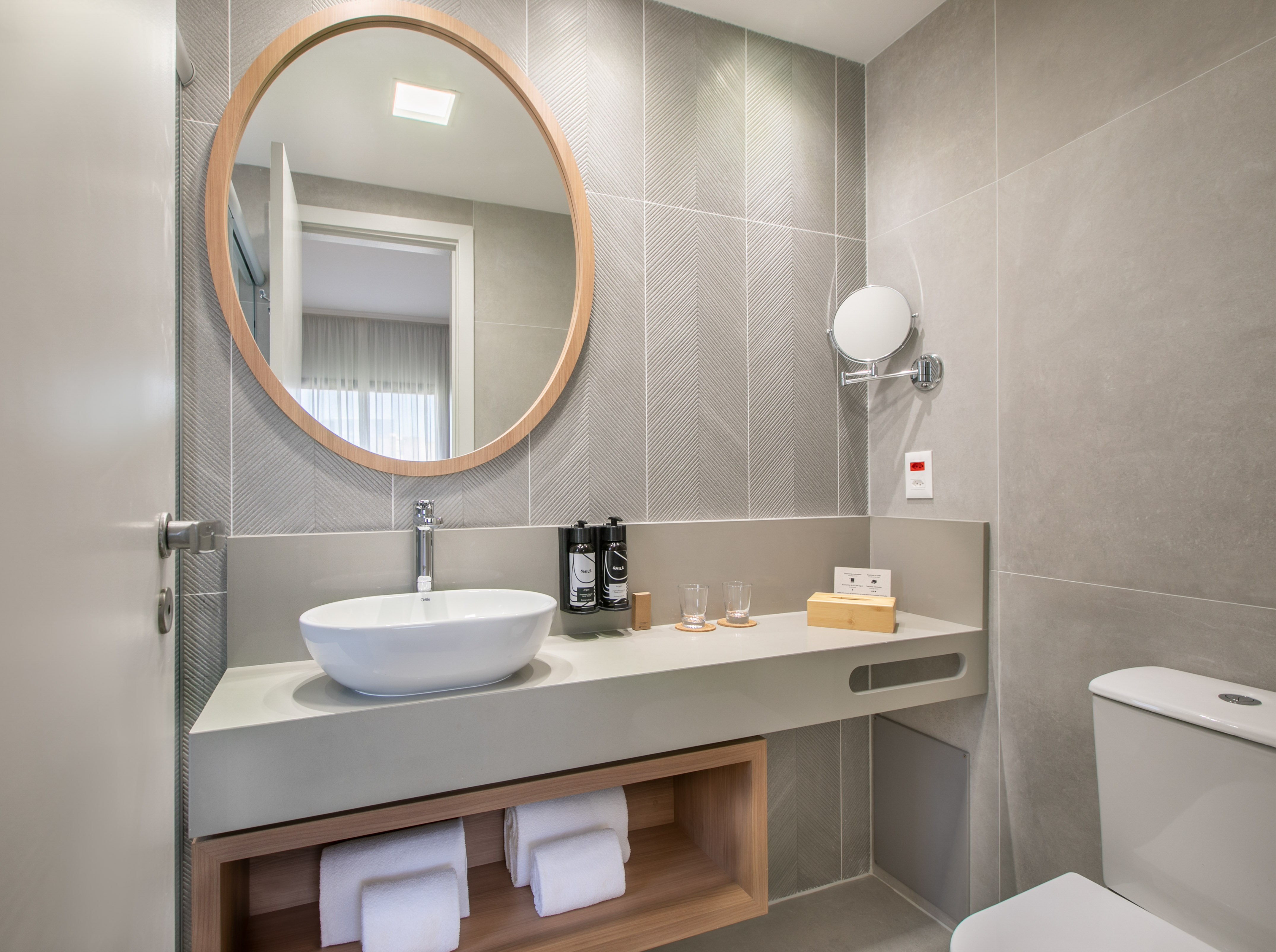 Modern bathroom with vessel sink, round mirror, grey chevron tiles, wooden vanity.