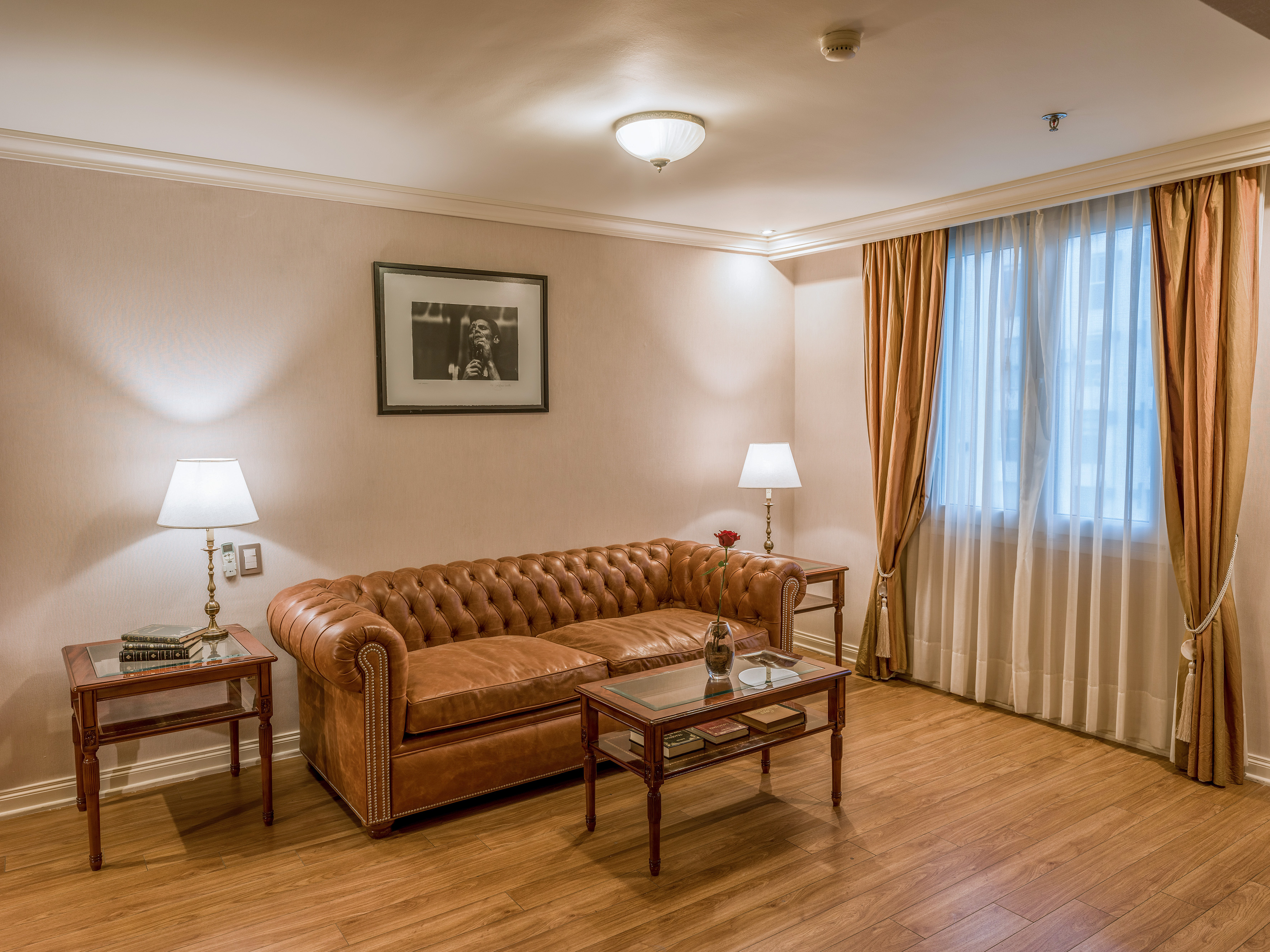 Elegant hotel living room with tufted brown leather sofa, lamps, and wood floor.