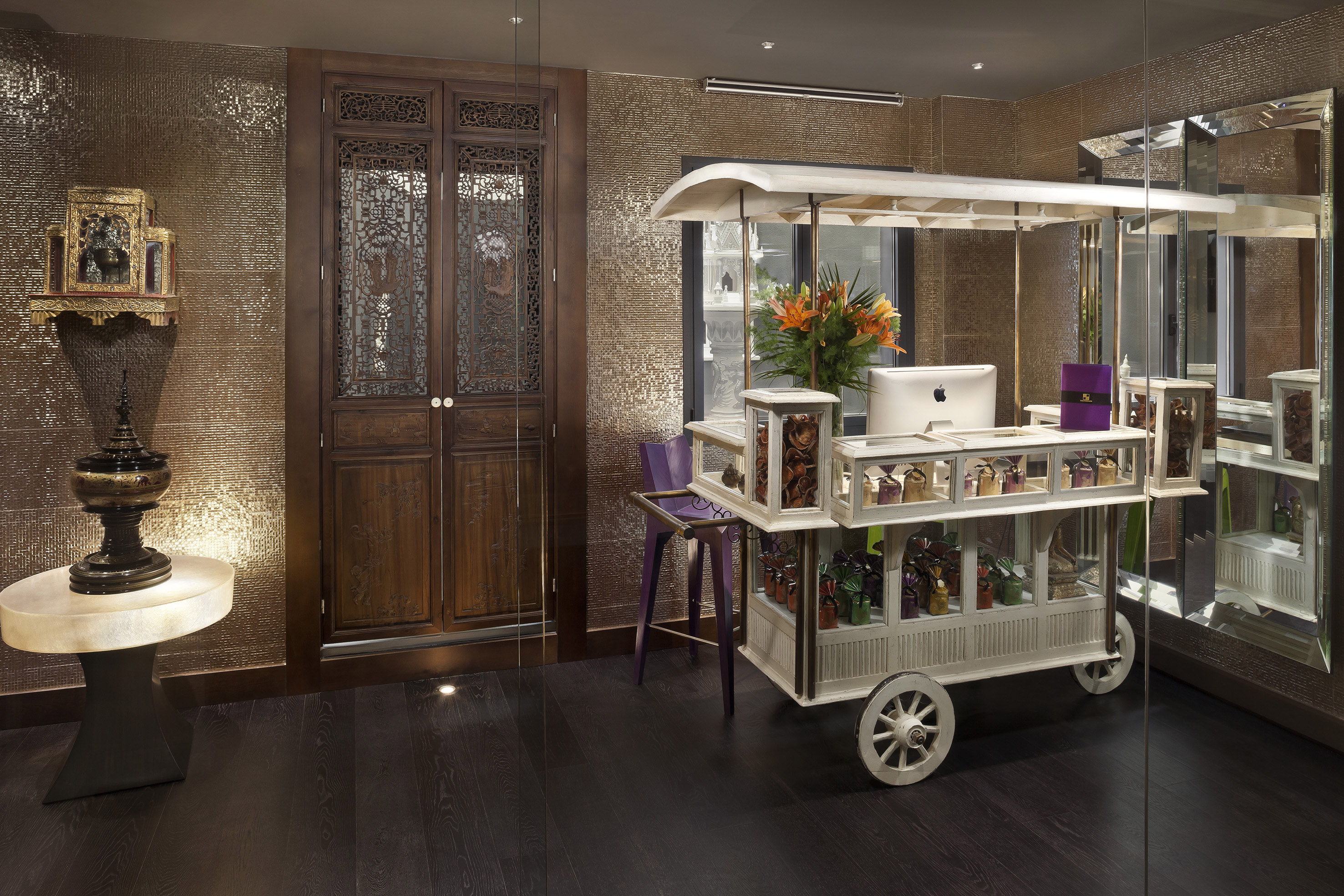 Luxury hotel lobby with vintage display cart, carved doors, and golden walls.