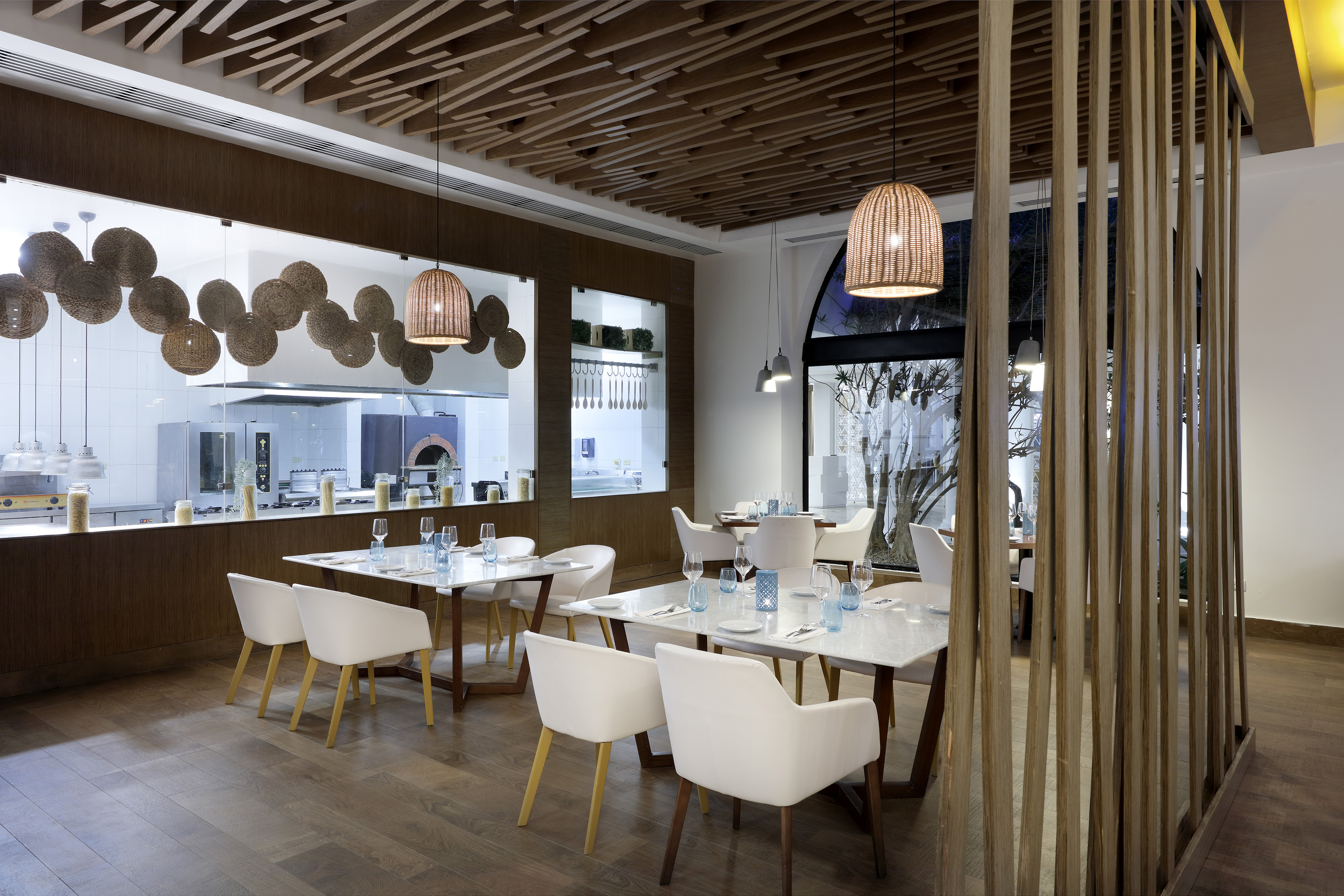 Modern restaurant dining room with open kitchen, wood design, and rattan lamps.