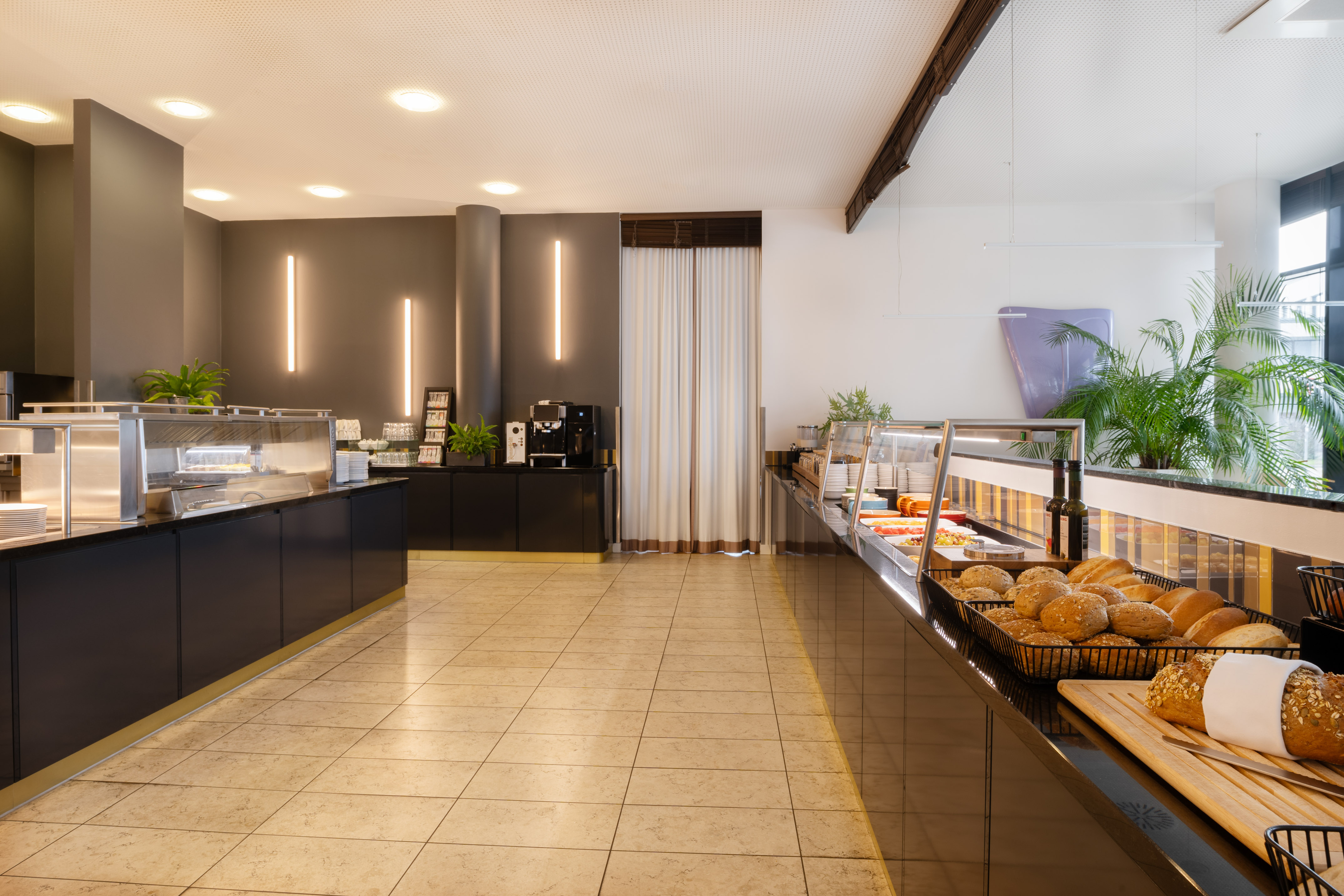 Modern hotel breakfast buffet with food stations, fresh bread, and coffee machine.