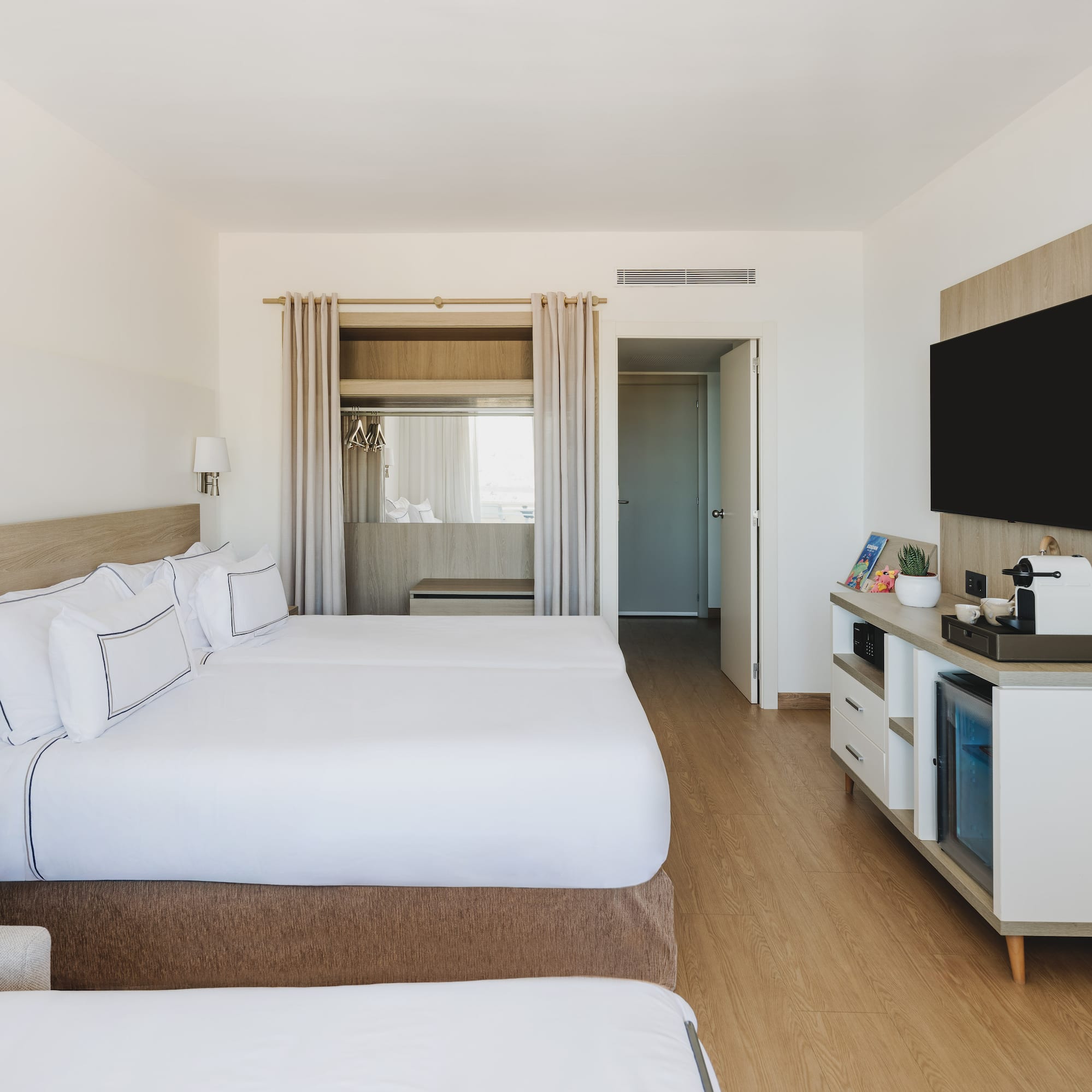 Moderna habitación de hotel con dos camas, TV y minibar. Interior luminoso.