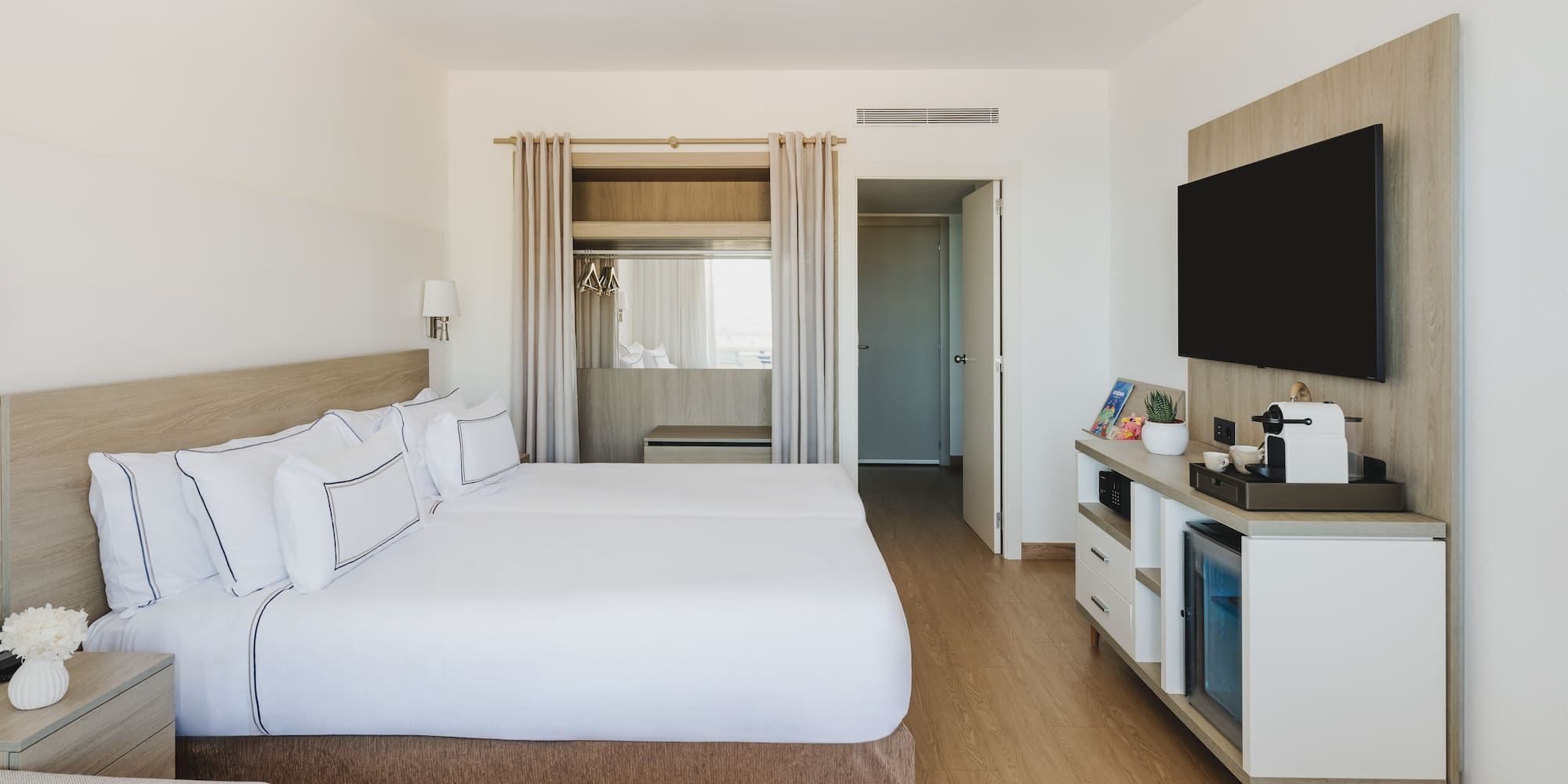 Moderna habitación de hotel con dos camas, TV y minibar. Interior luminoso.