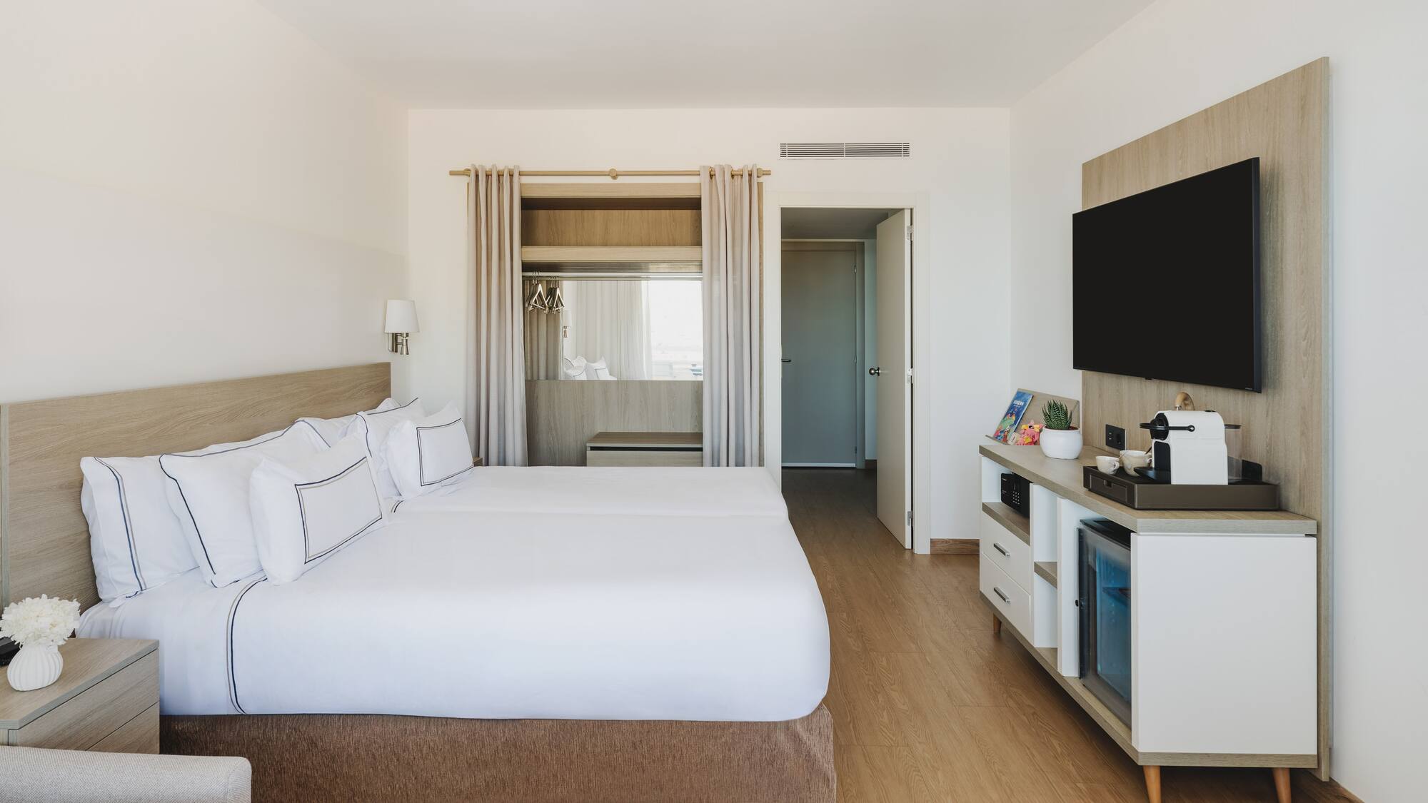 Moderna habitación de hotel con dos camas, TV y minibar. Interior luminoso.