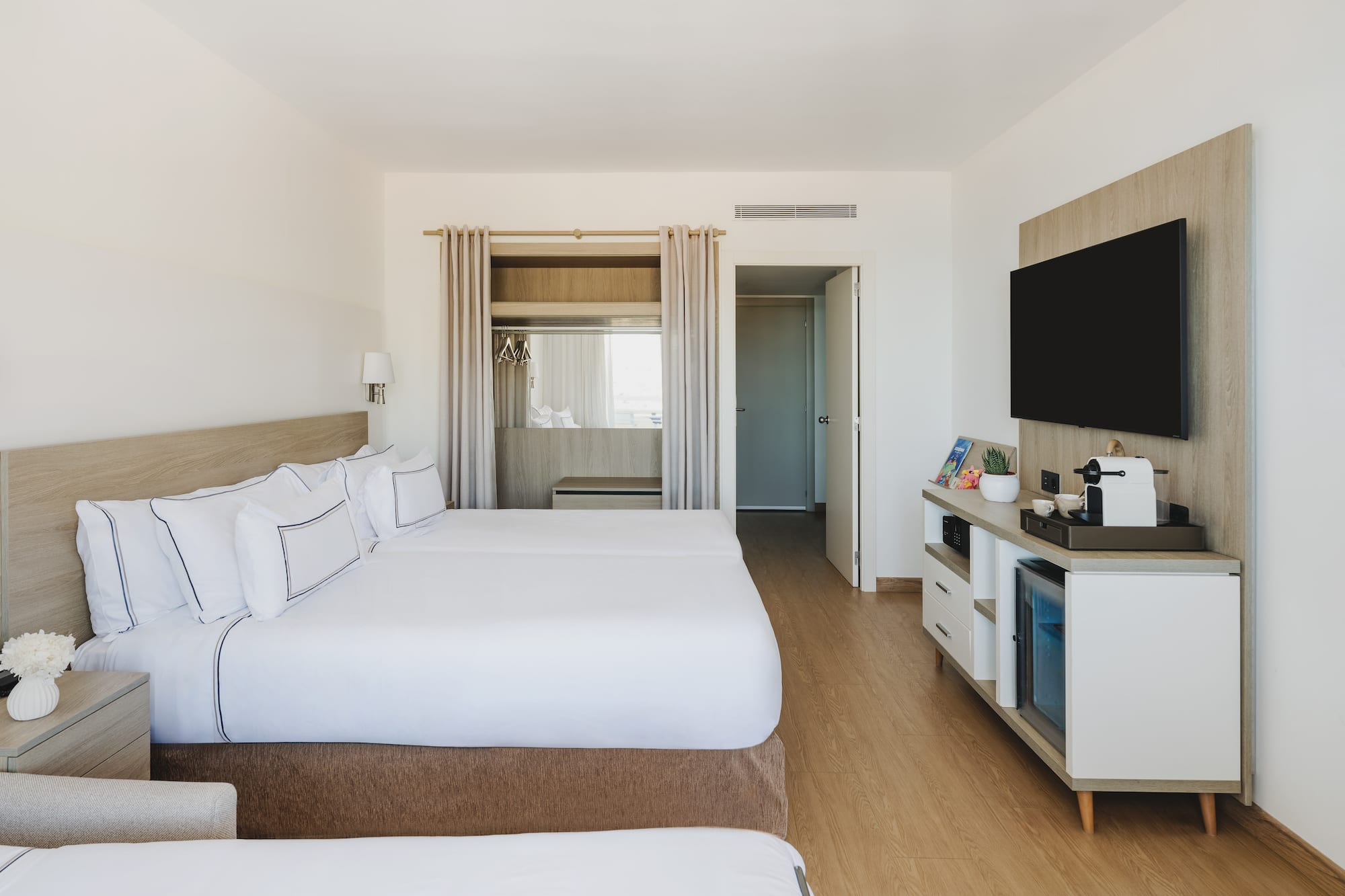 Moderna habitación de hotel con dos camas, TV y minibar. Interior luminoso.