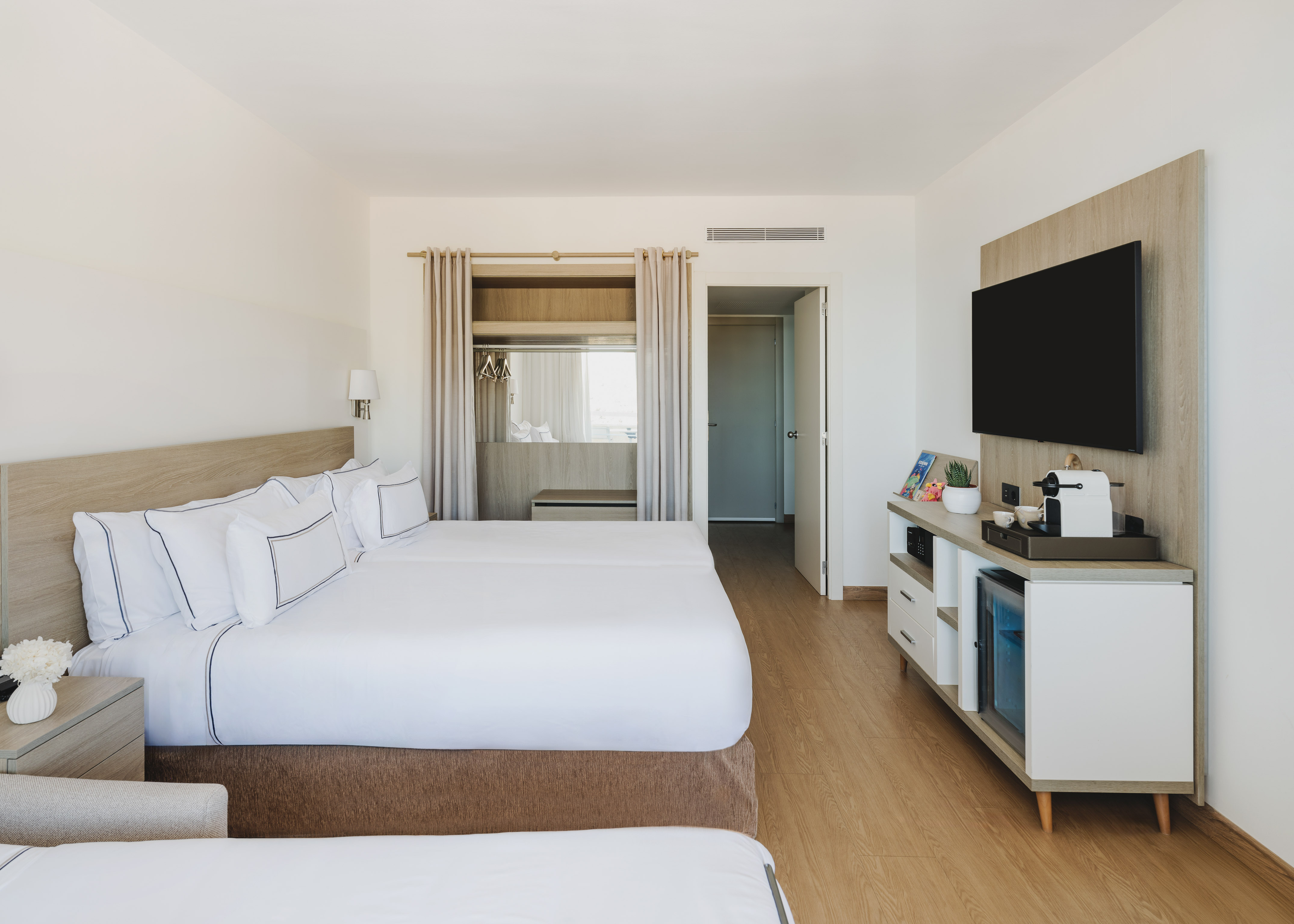Moderna habitación de hotel con dos camas, TV y minibar. Interior luminoso.