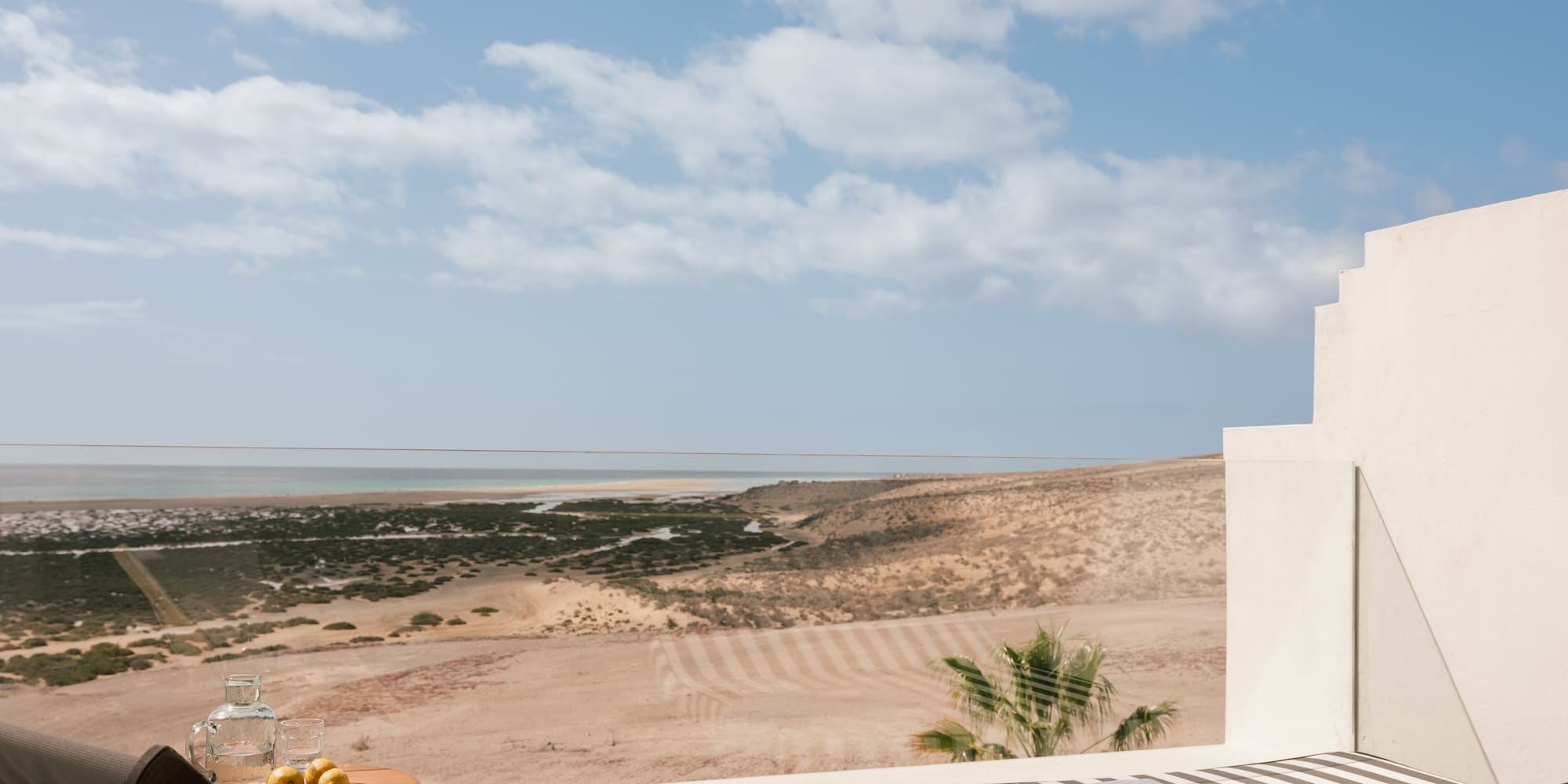 Terraza de hotel con vista al mar y desierto, tumbonas, libro y limones.