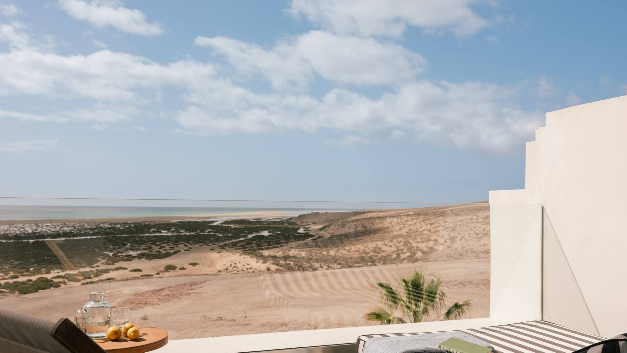 Terraza de hotel con vista al mar y desierto, tumbonas, libro y limones.