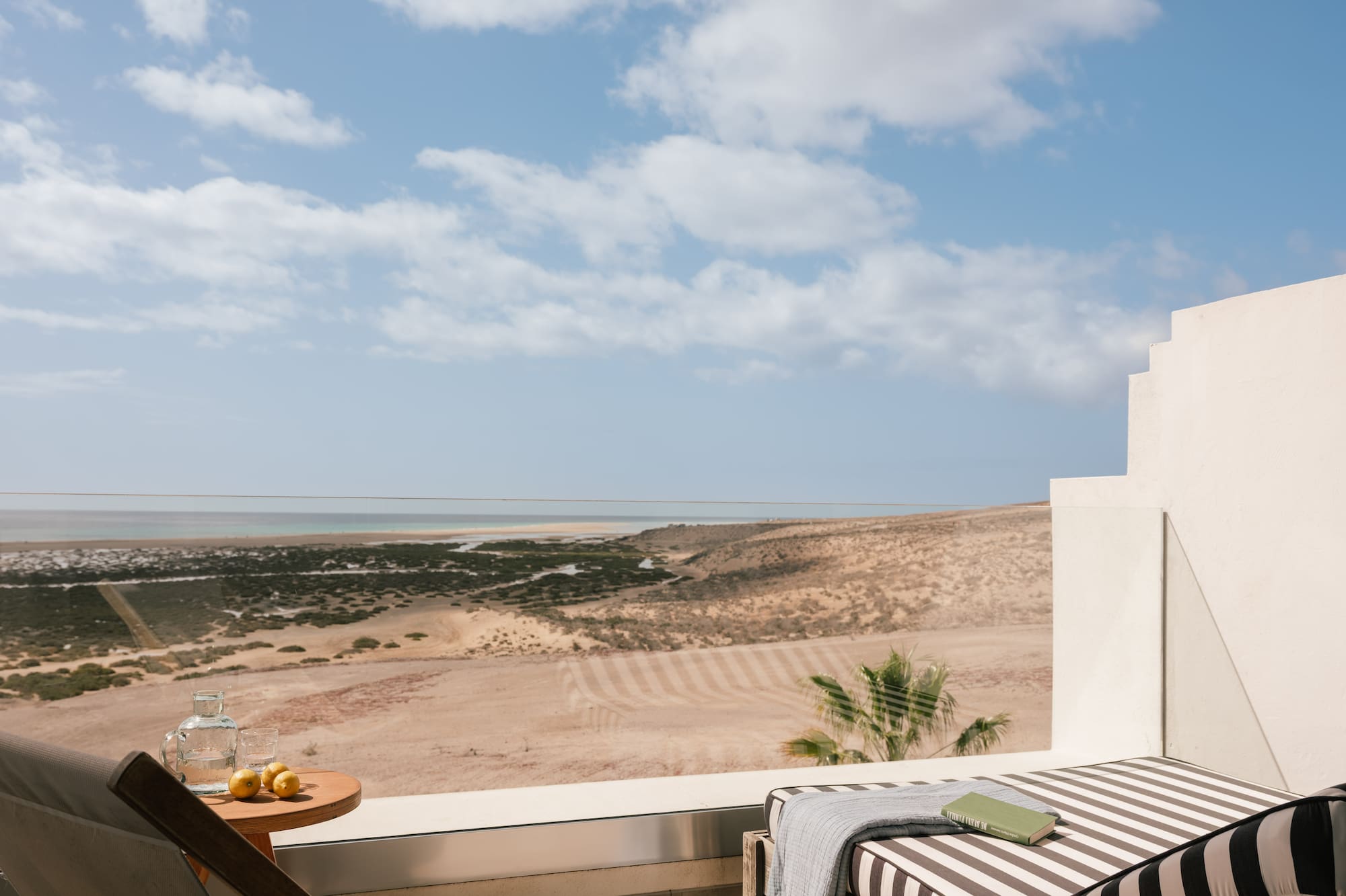 Terraza de hotel con vista al mar y desierto, tumbonas, libro y limones.
