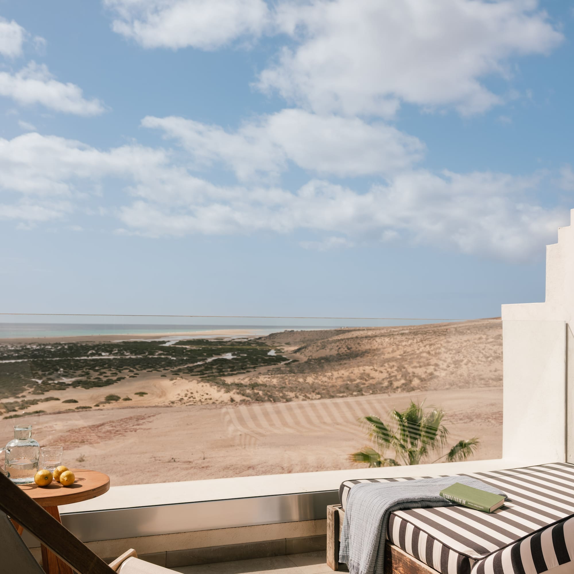 Terraza de hotel con vista al mar y desierto, tumbonas, libro y limones.