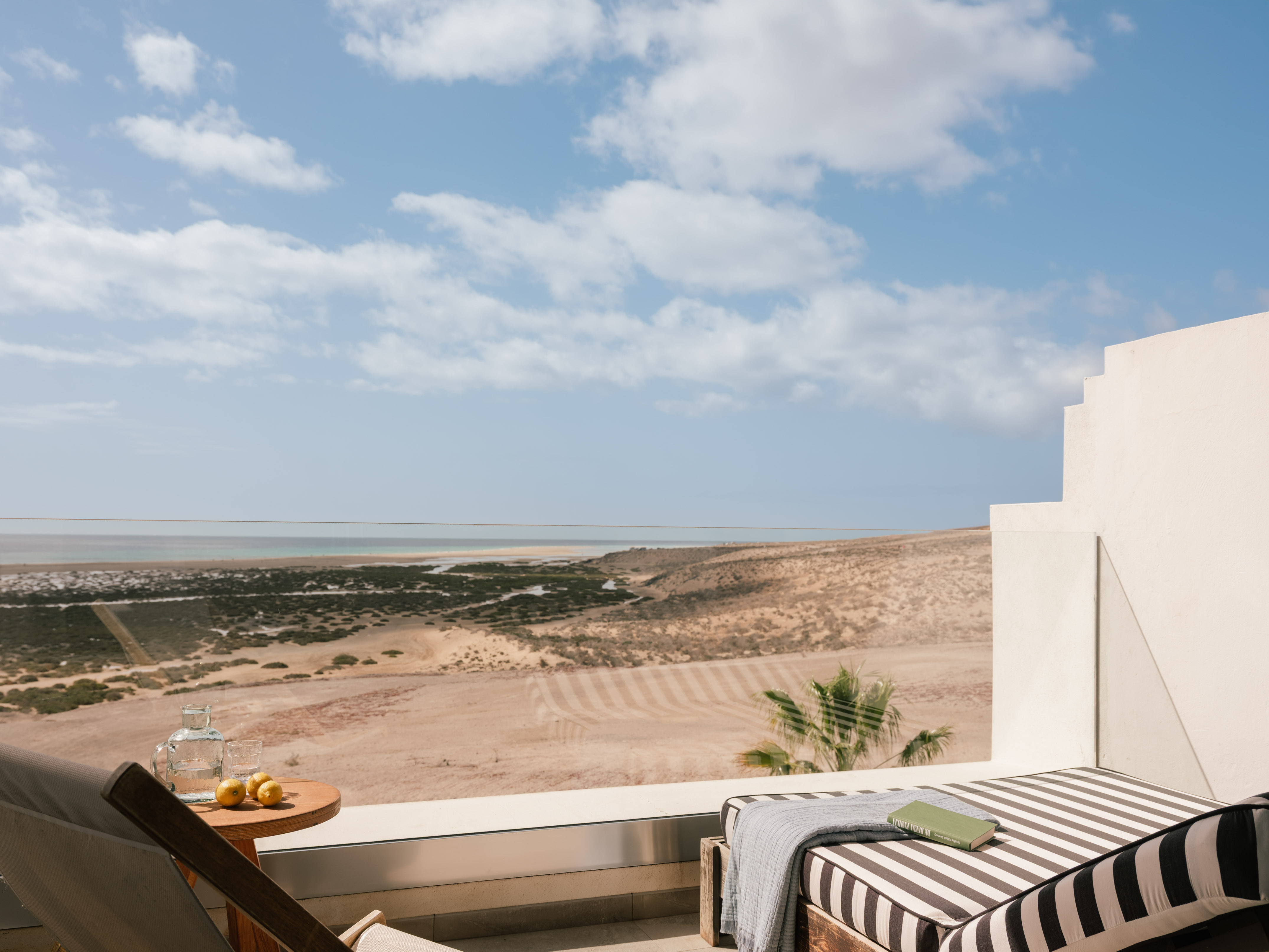 Terraza de hotel con vista al mar y desierto, tumbonas, libro y limones.