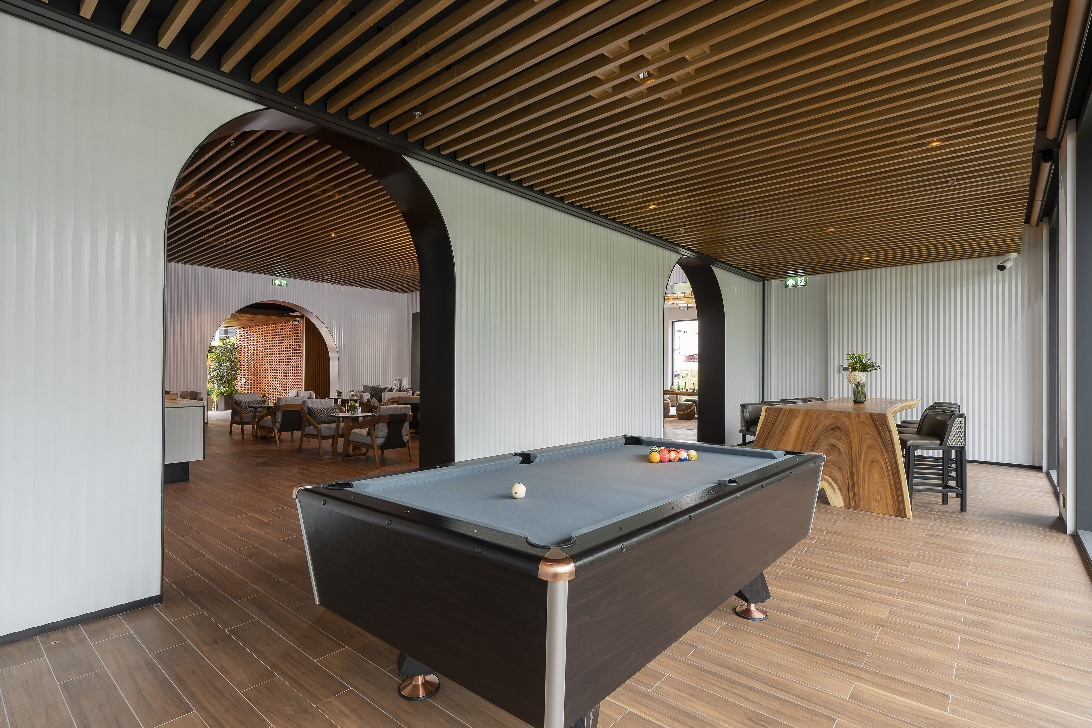 Modern recreation room with pool table, wood slat ceiling, and arched white walls.