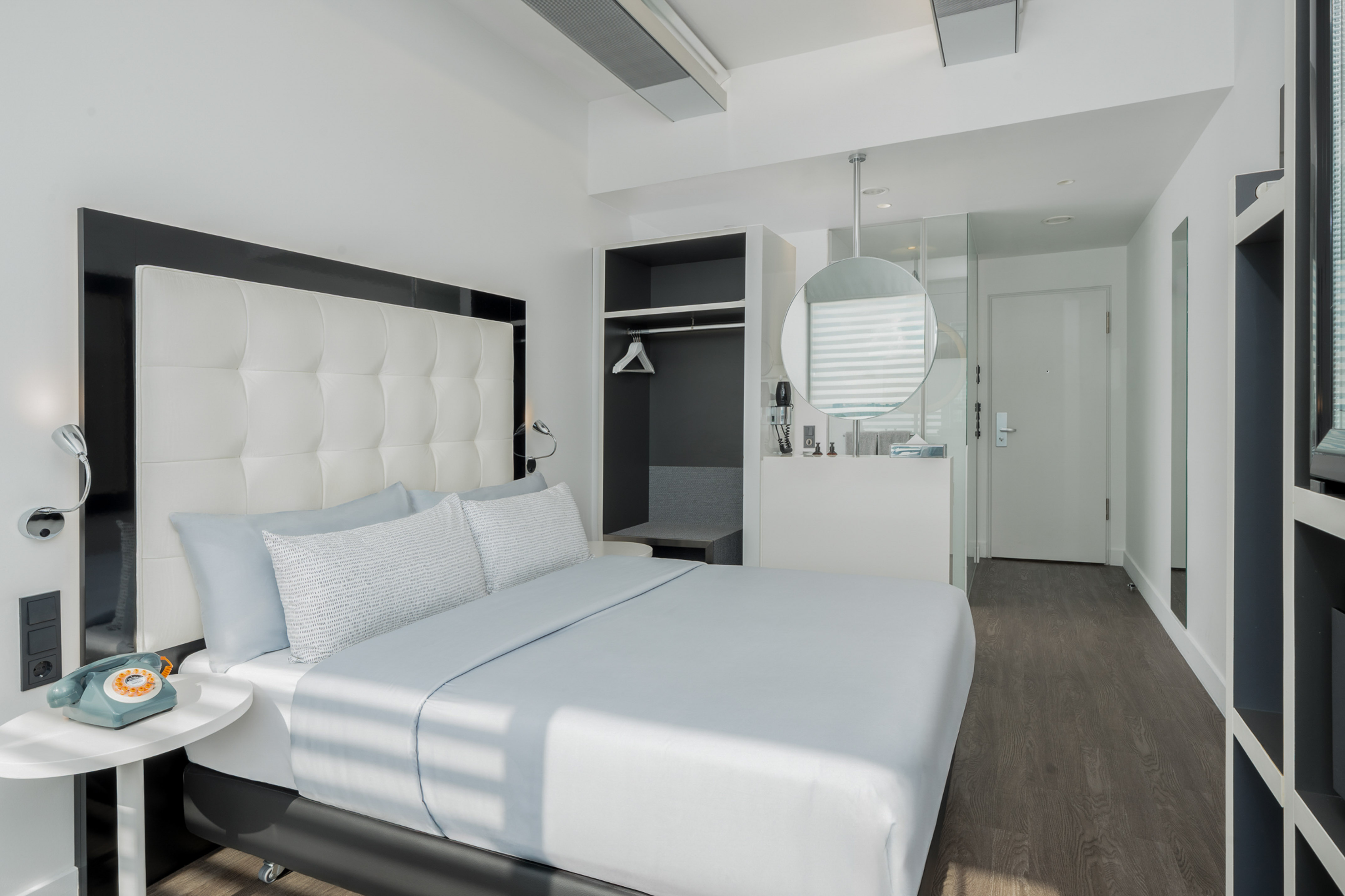 Modern hotel room: white tufted bed, light blue bedding, minimalist design.